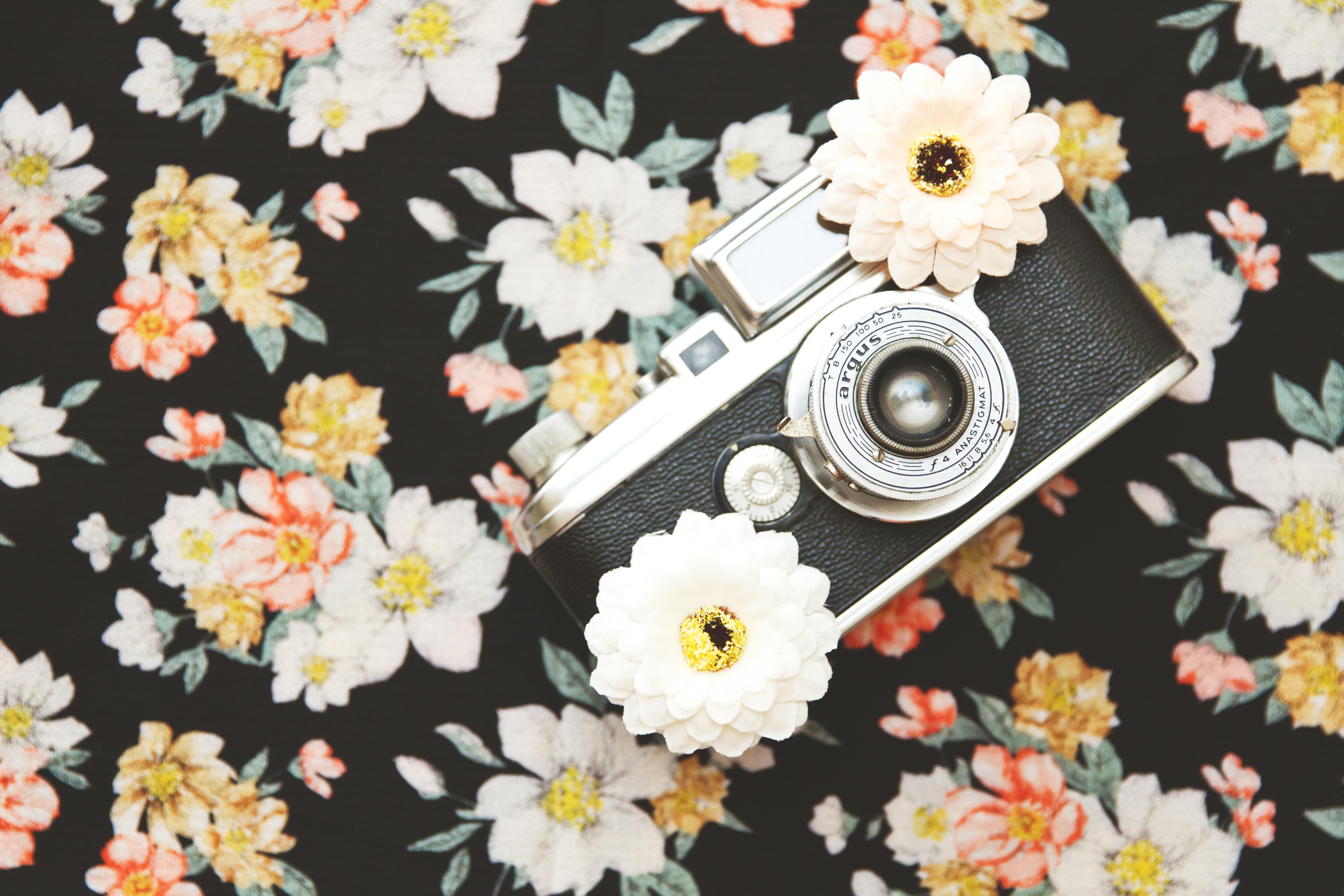 black and silver analogue SLR camera with white flowers