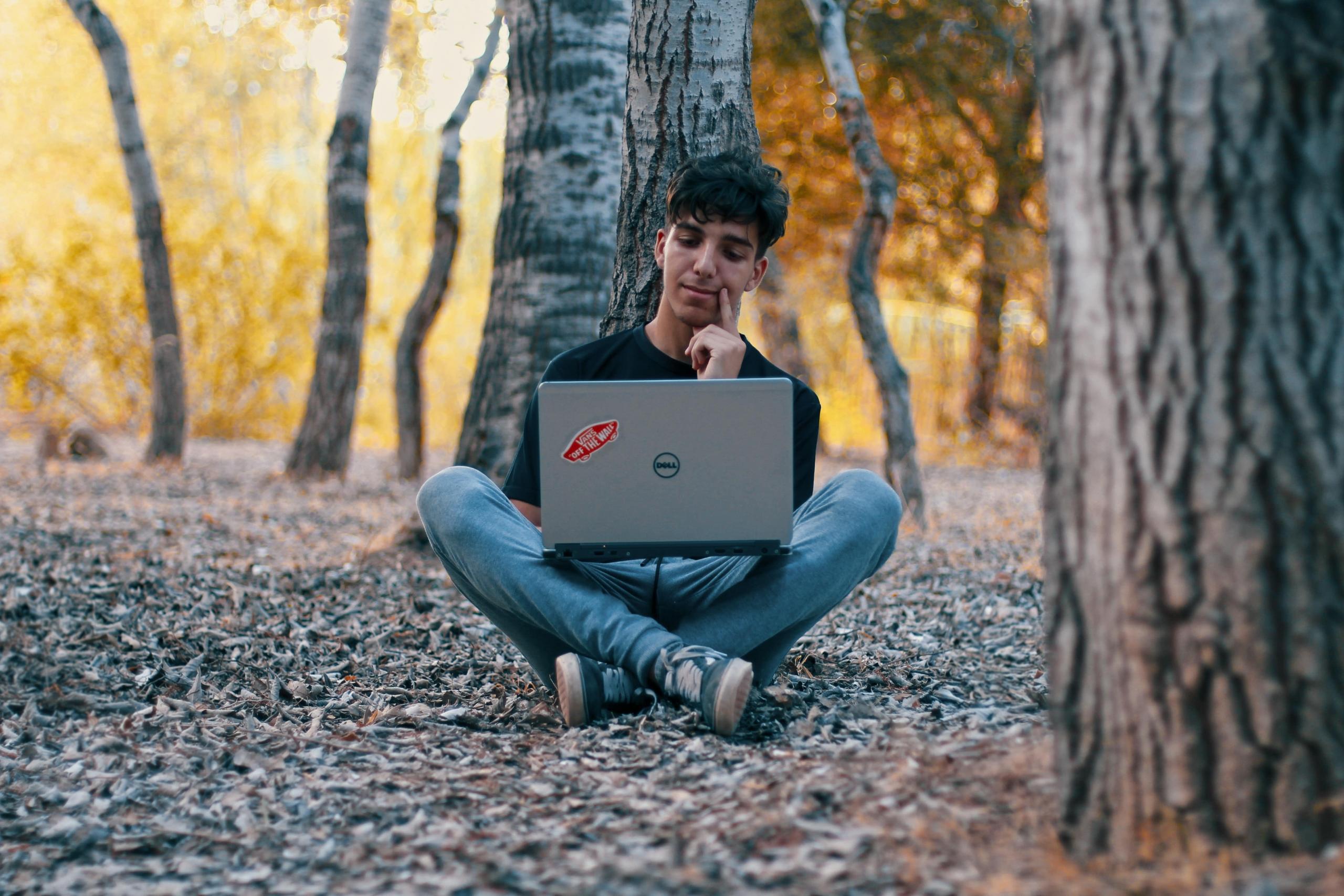 student seated outside under trees working on laptop