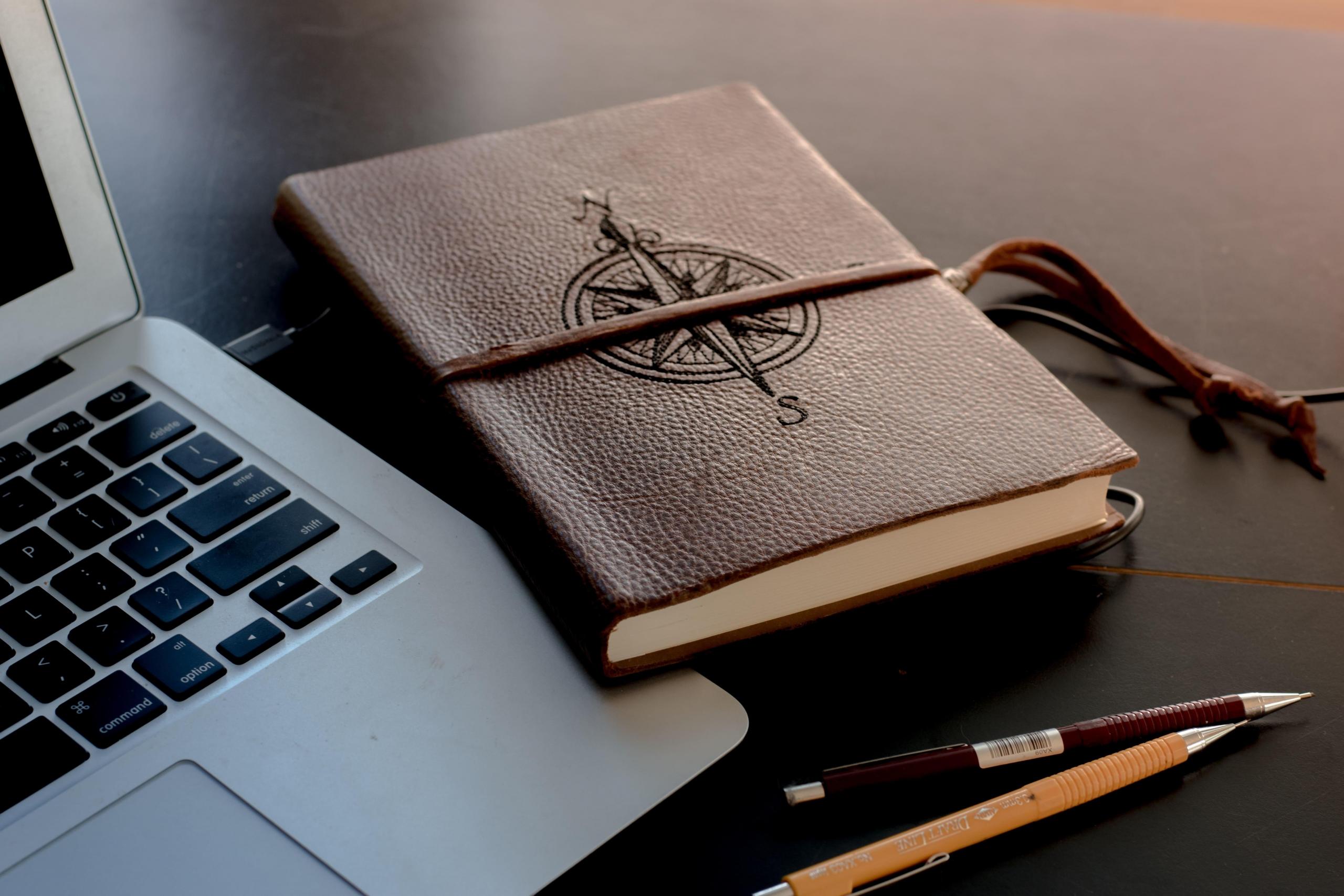 notebook embossed with four points of compass next to laptop