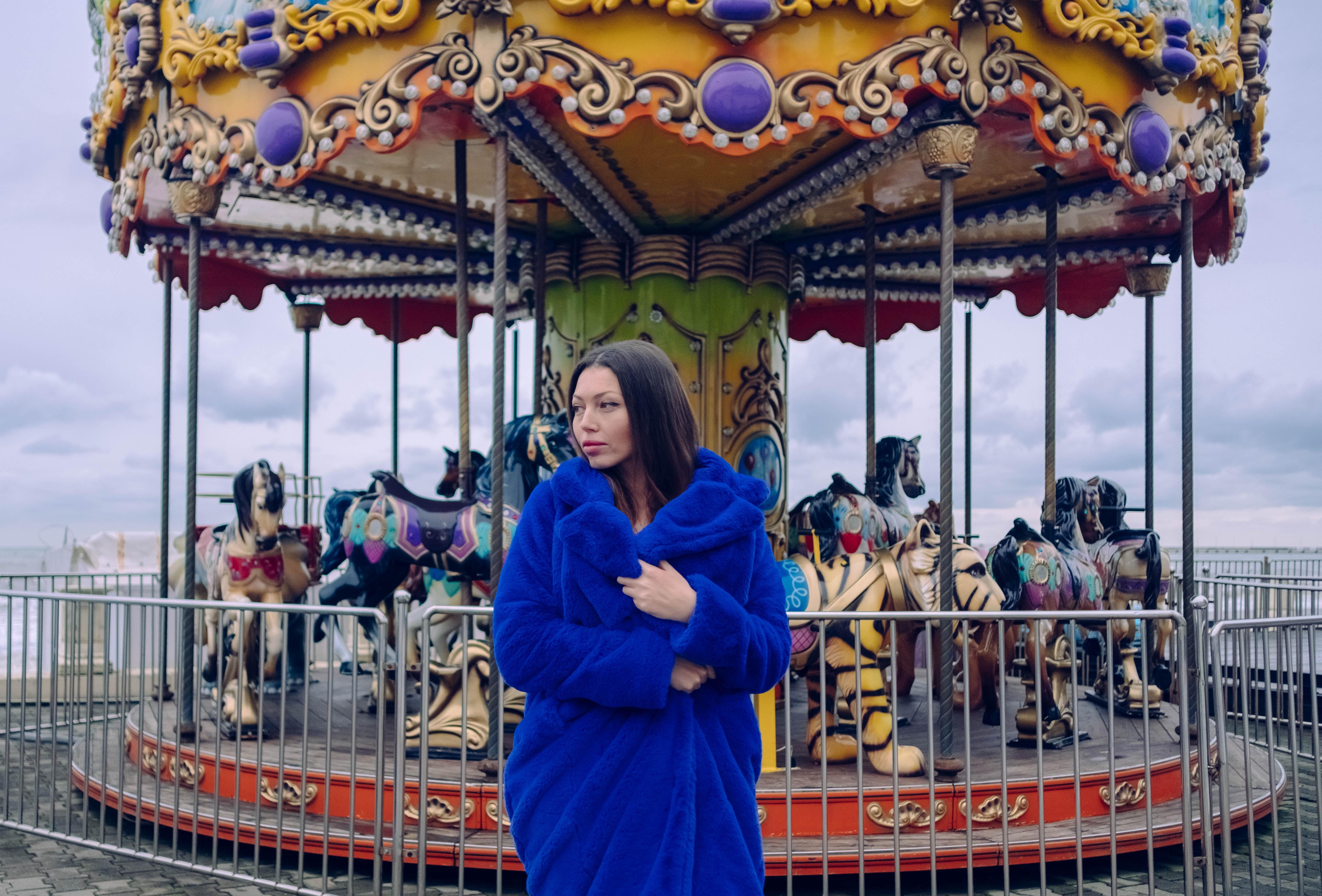woman in blue coat standing in front of carousel