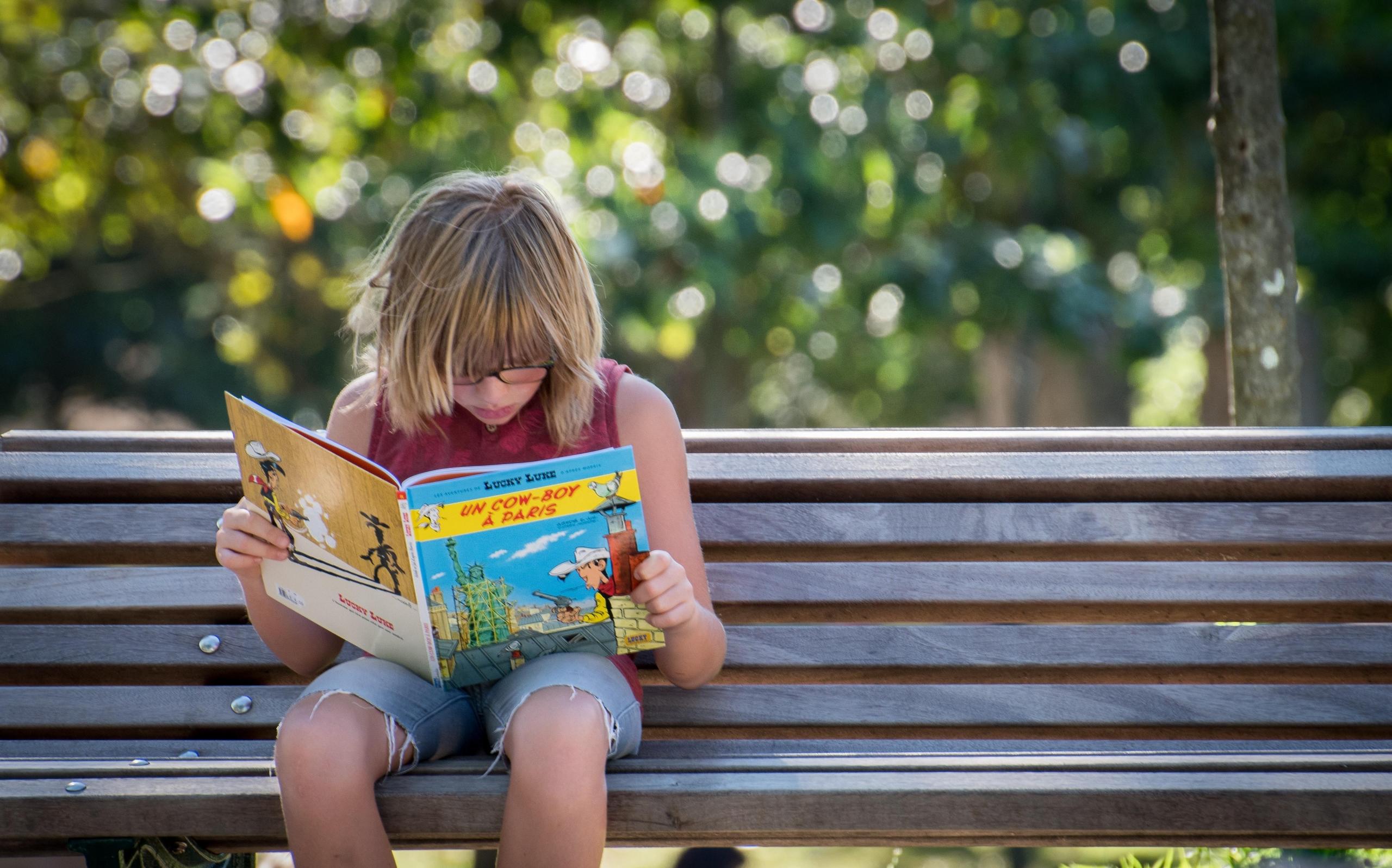 girl in red top sitting on bench while reading a French book