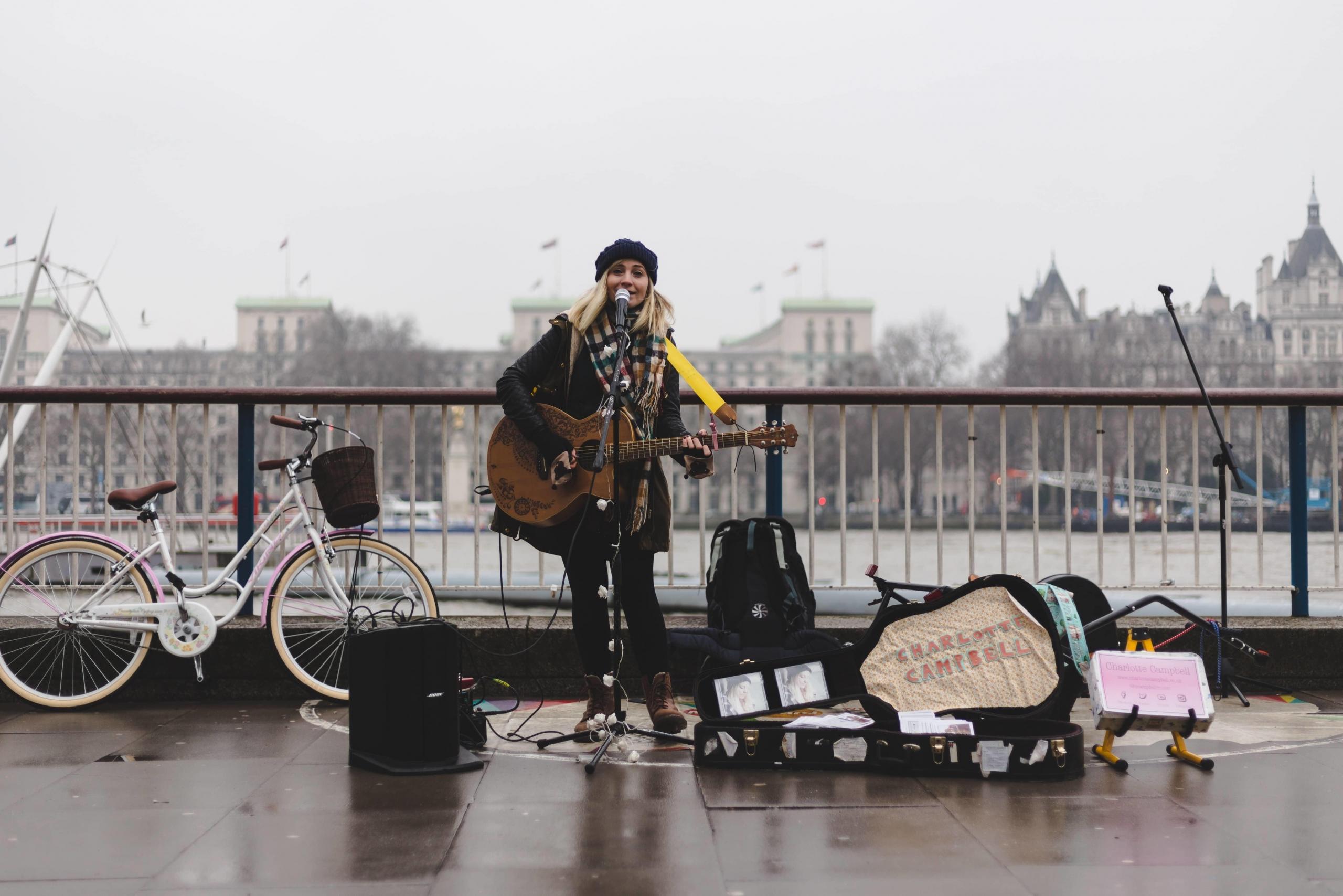 woman playing guitar and singing outside on a bridge