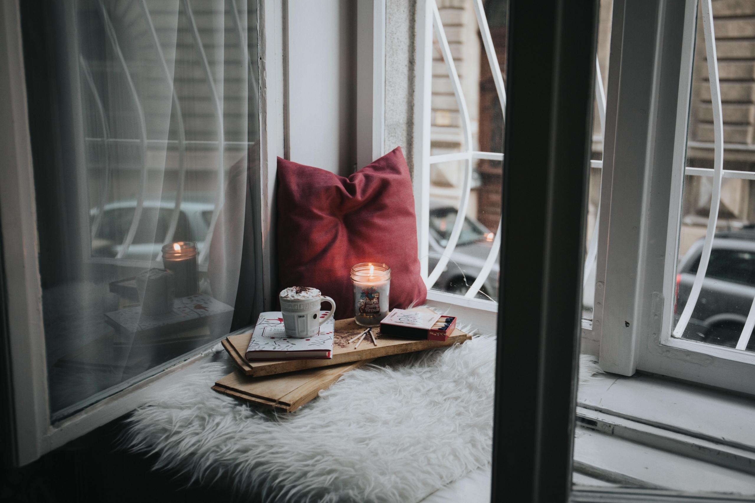 candle, mug, journal and cushion on windowsill