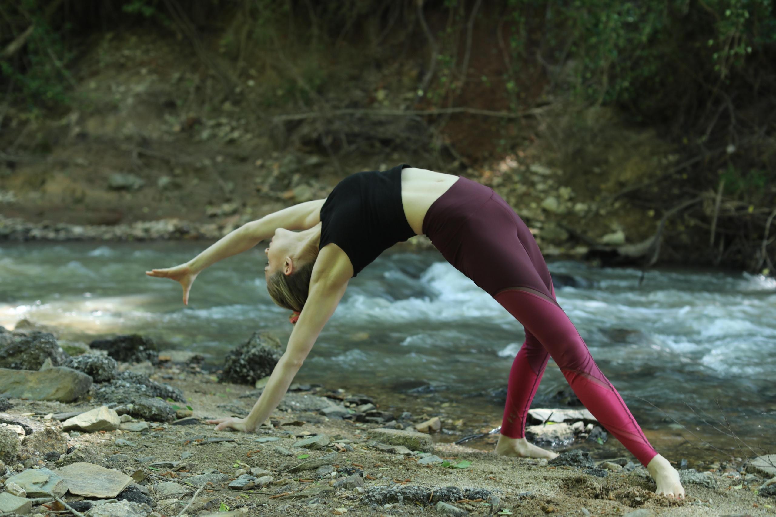 woman doing reverse downward facing dog yoga pose near stream