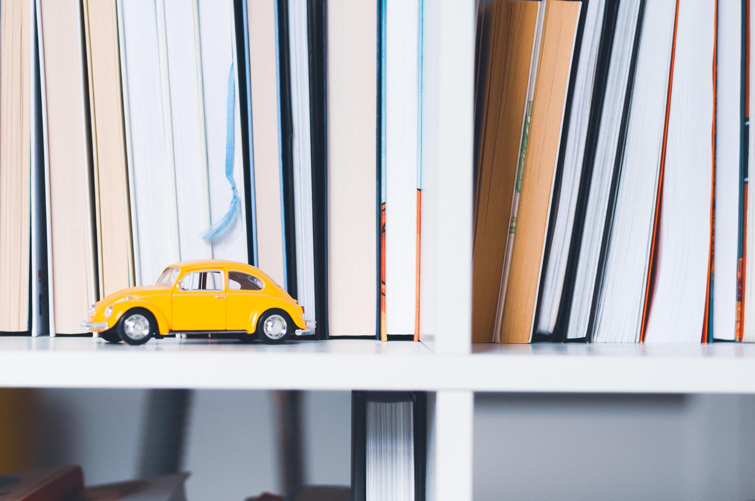 yellow toy car on bookshelf with books