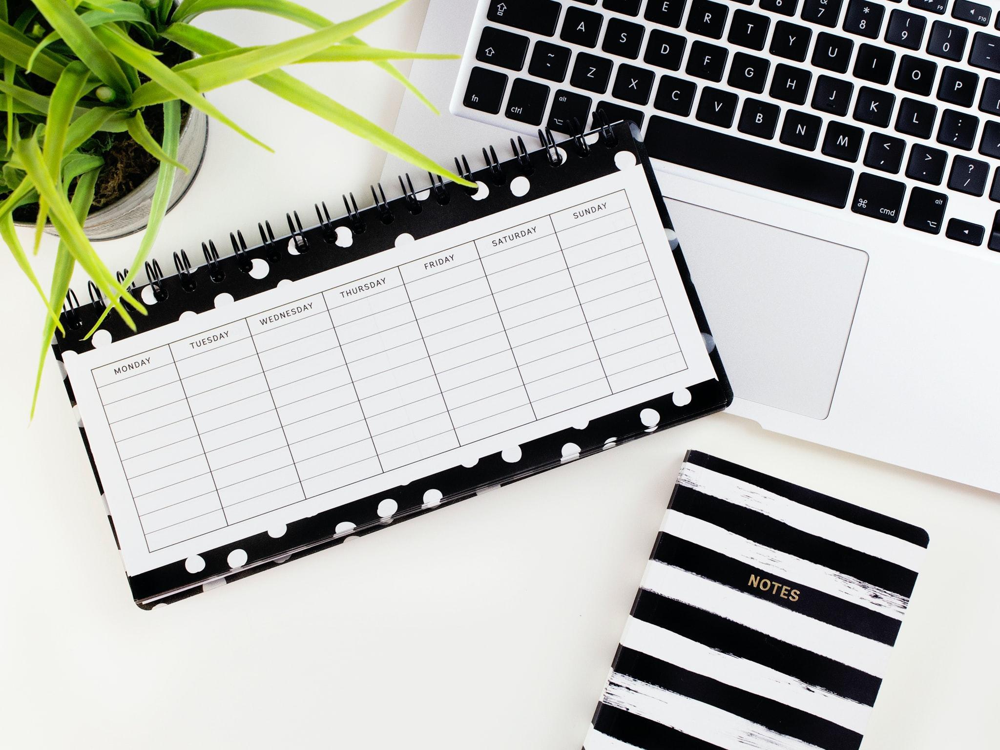 black and white planner, striped notebookand laptop on desk
