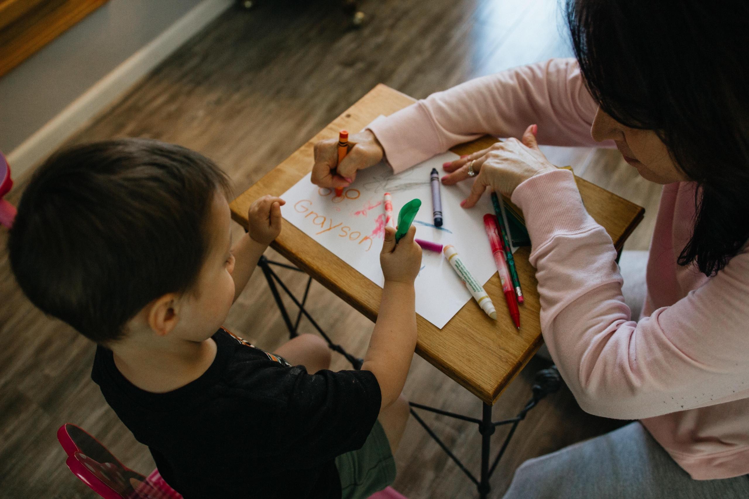 teacher teaching young boy to write with crayons