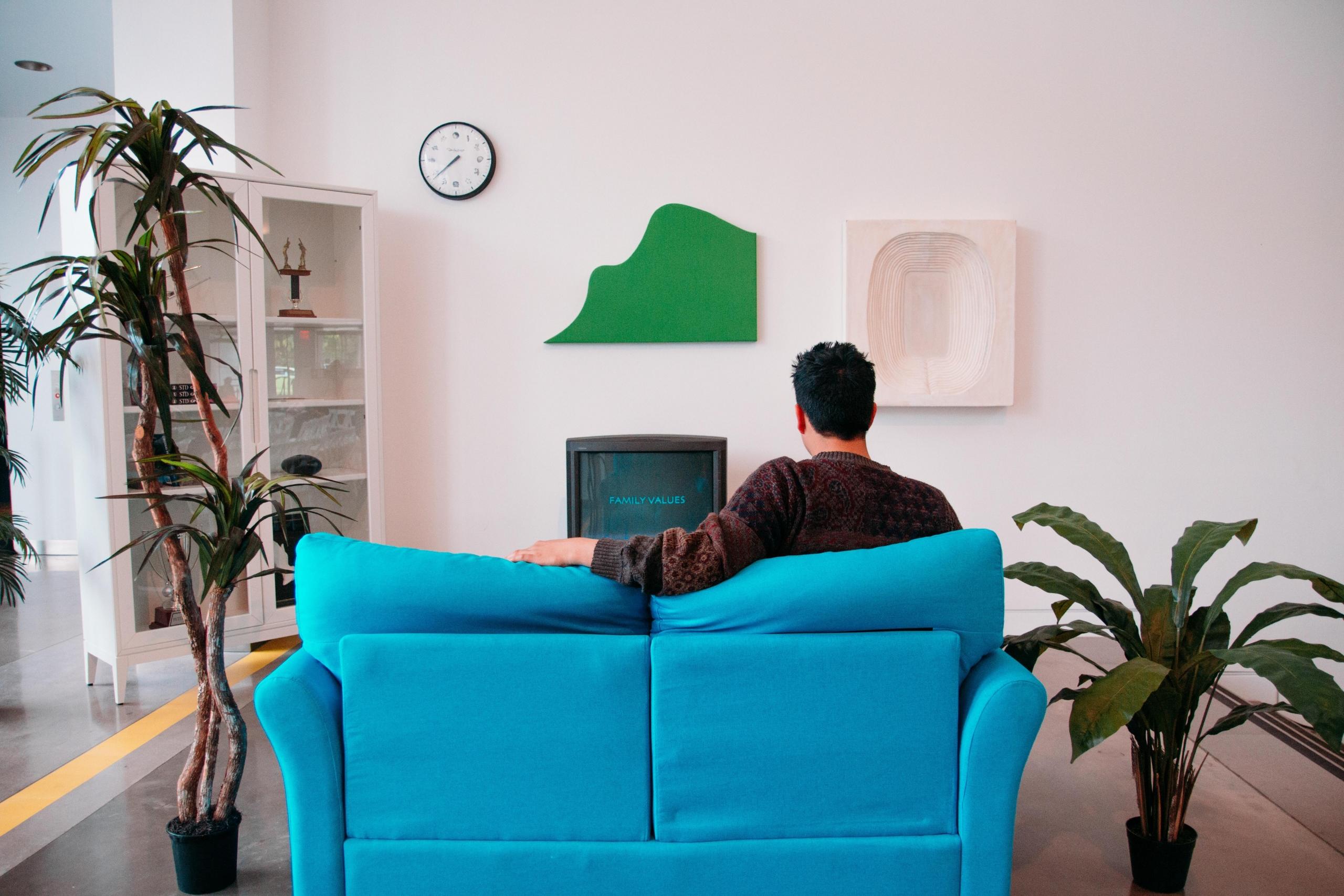 man on blue couch watching television