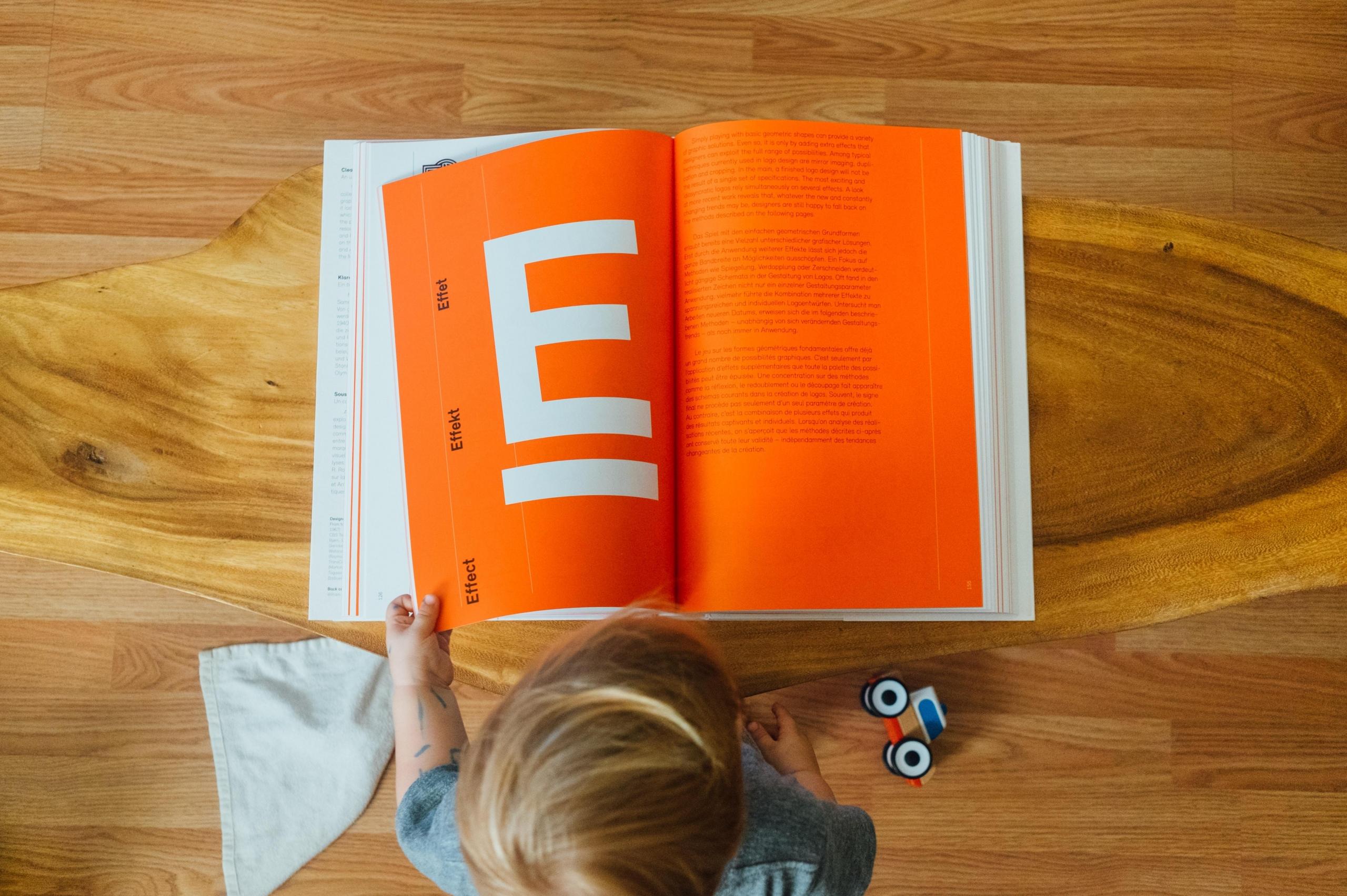 young child reading book with orange background