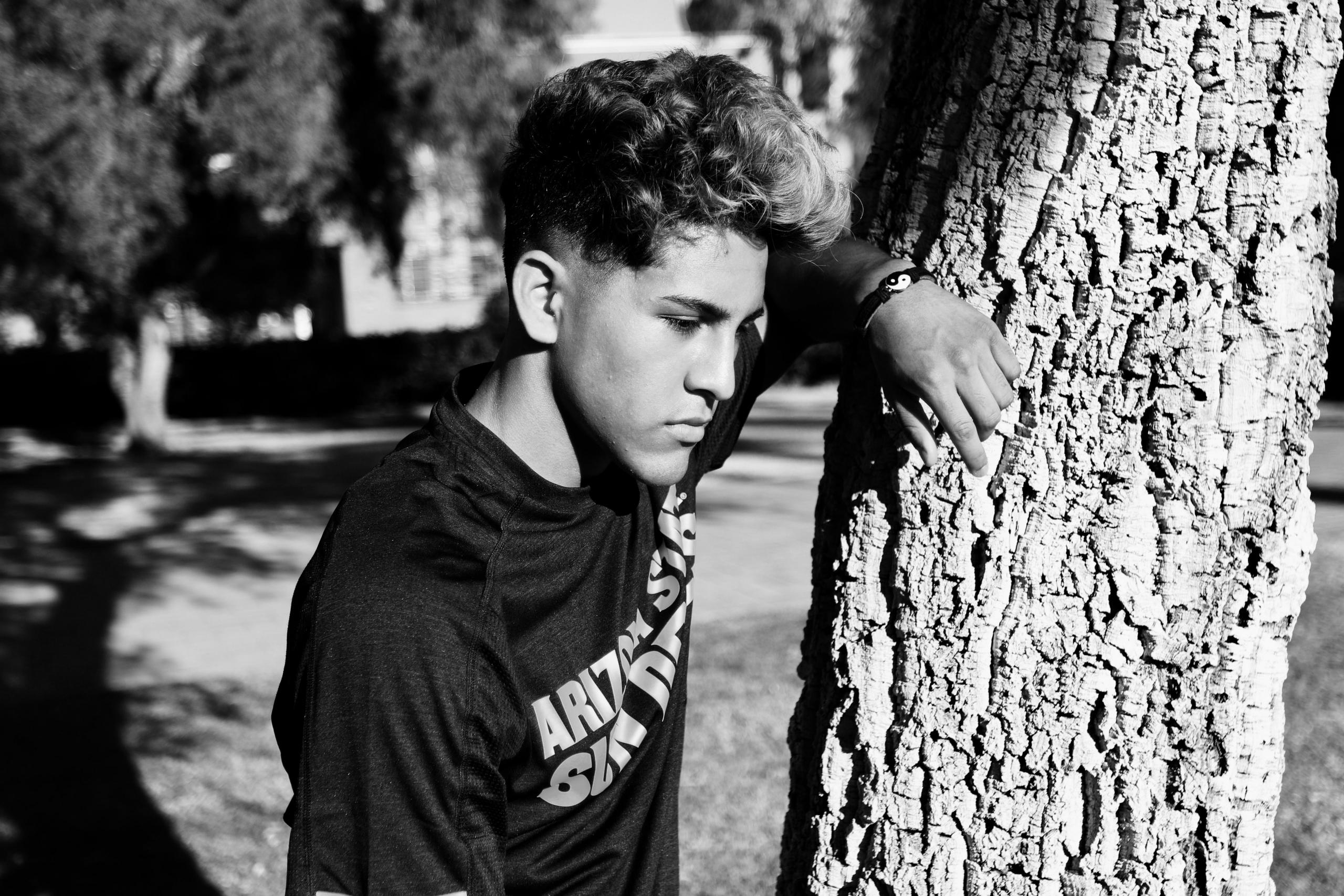 black and white image of pensive boy leaning againts tree