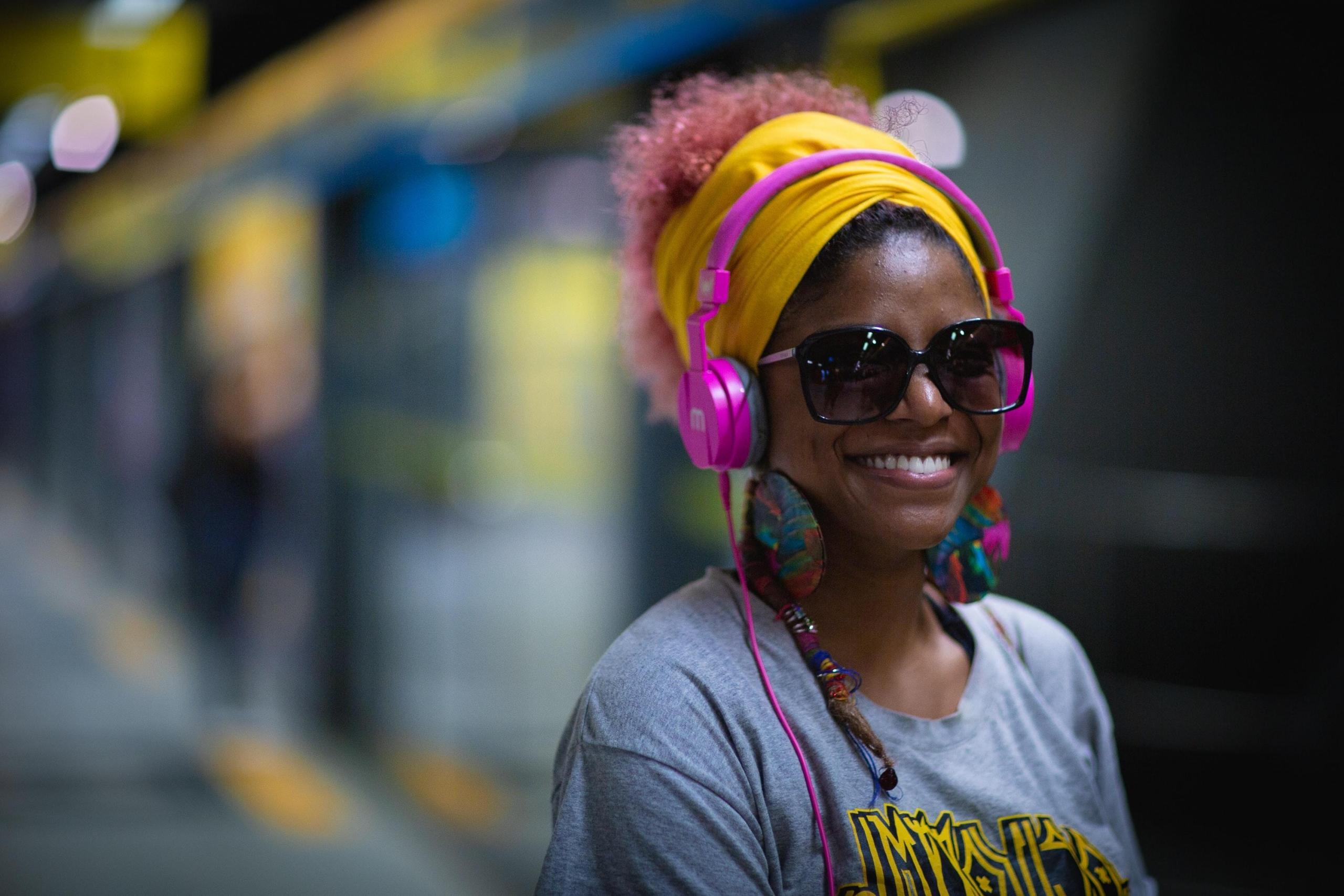 smiling woman wearing bright pink headphones at train station