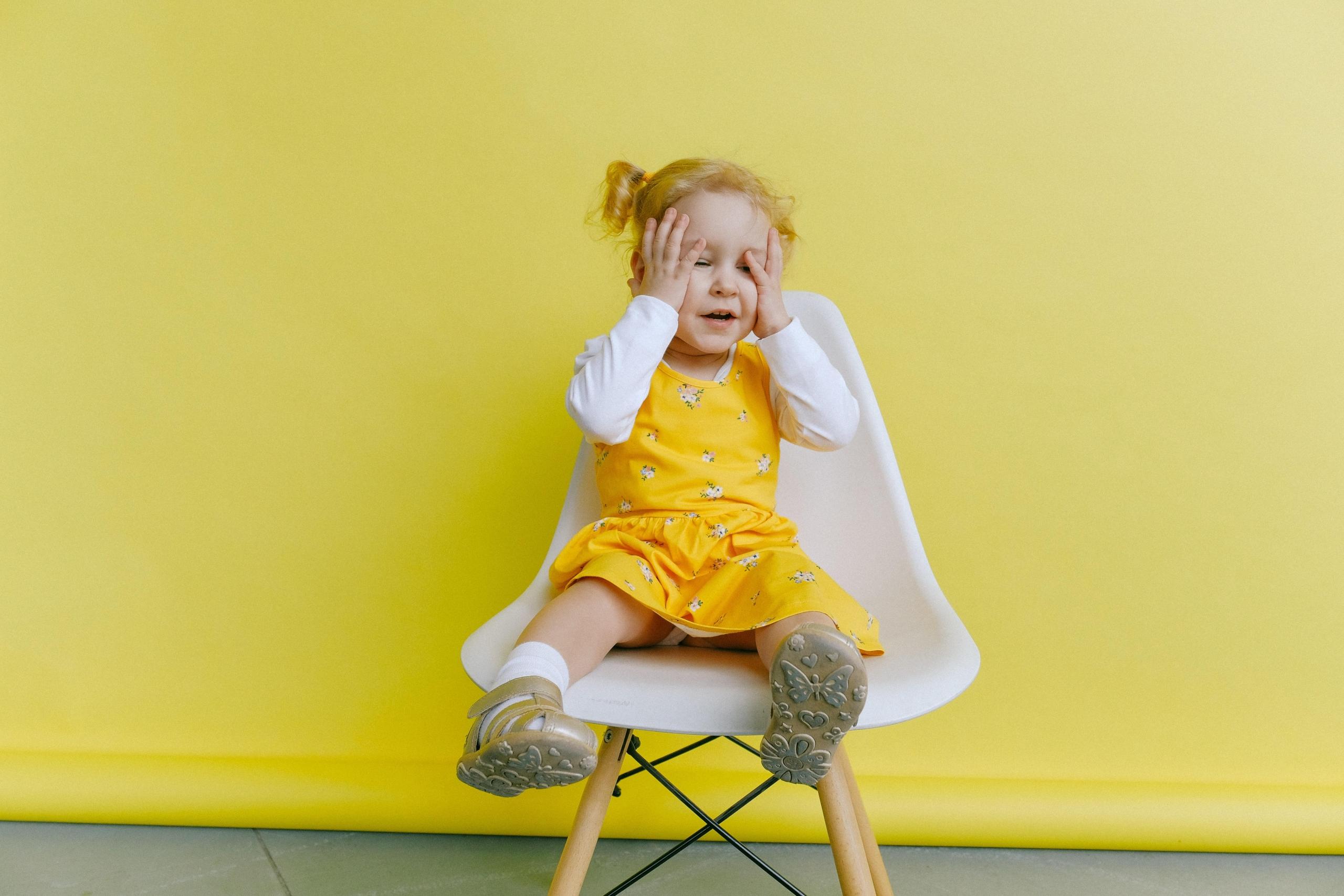 small girl seated on chair in front of yellow wall