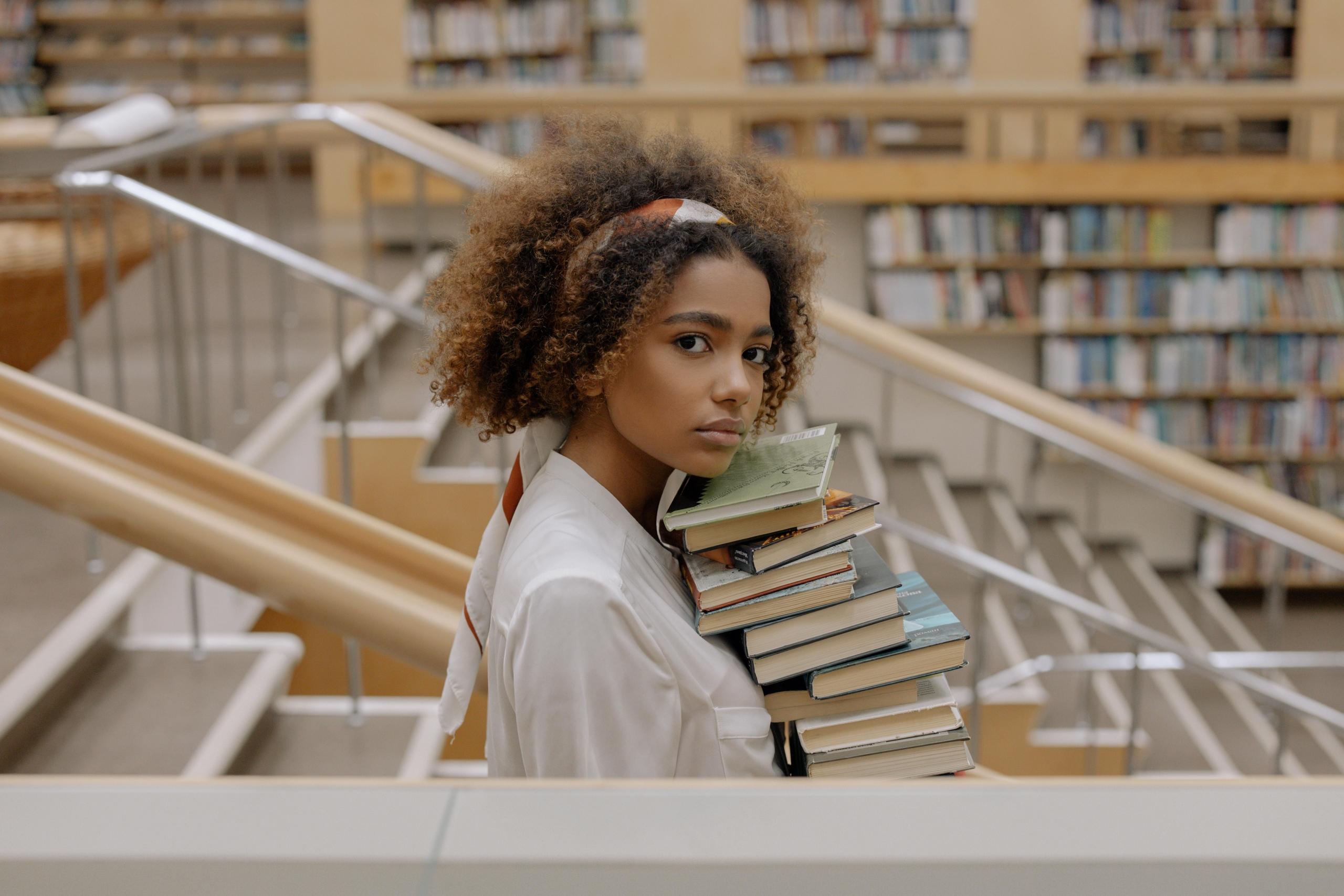 girl carrying a stack of books in library