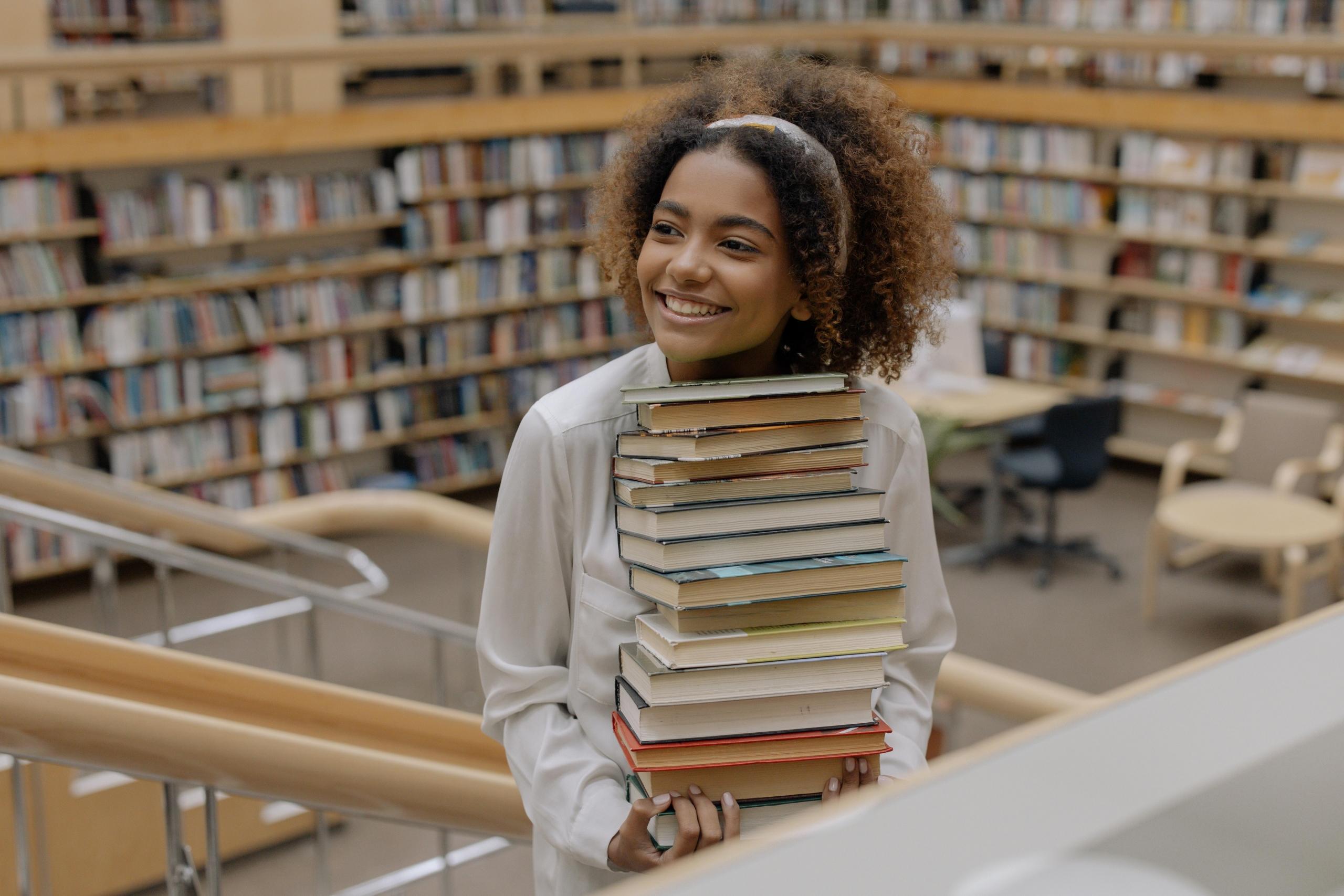 girl carrying a pile of books in library