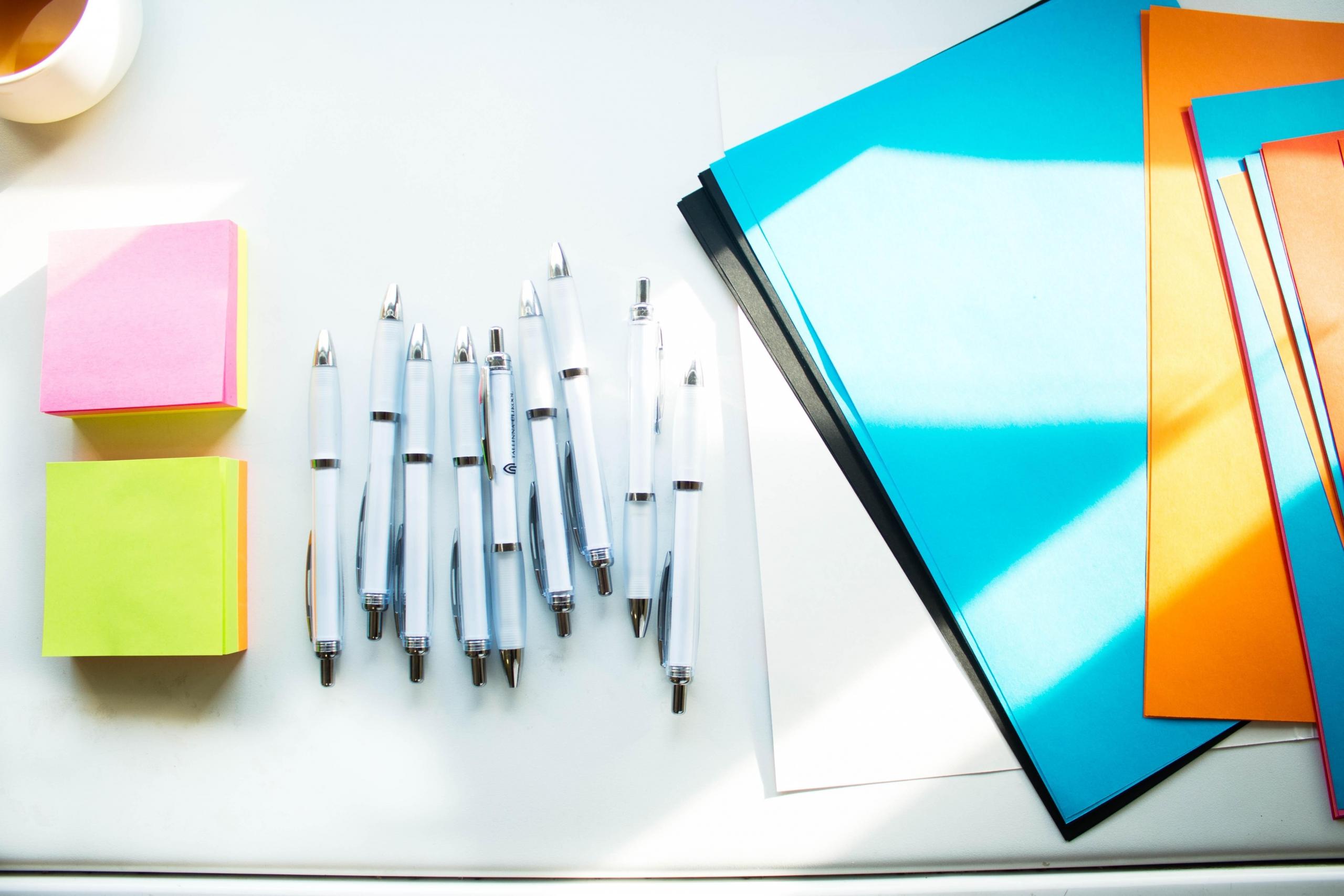 sheets of colourful paper, sticky notes and pens on desk