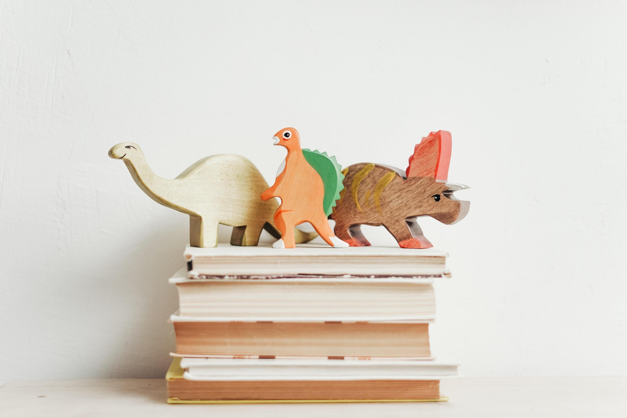 pile of books topped with toy dinosaurs