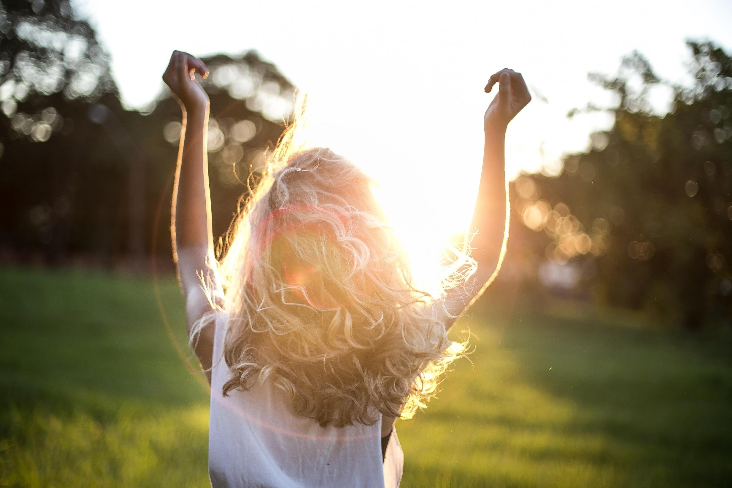 woman with back to camera raising her arms to the sky