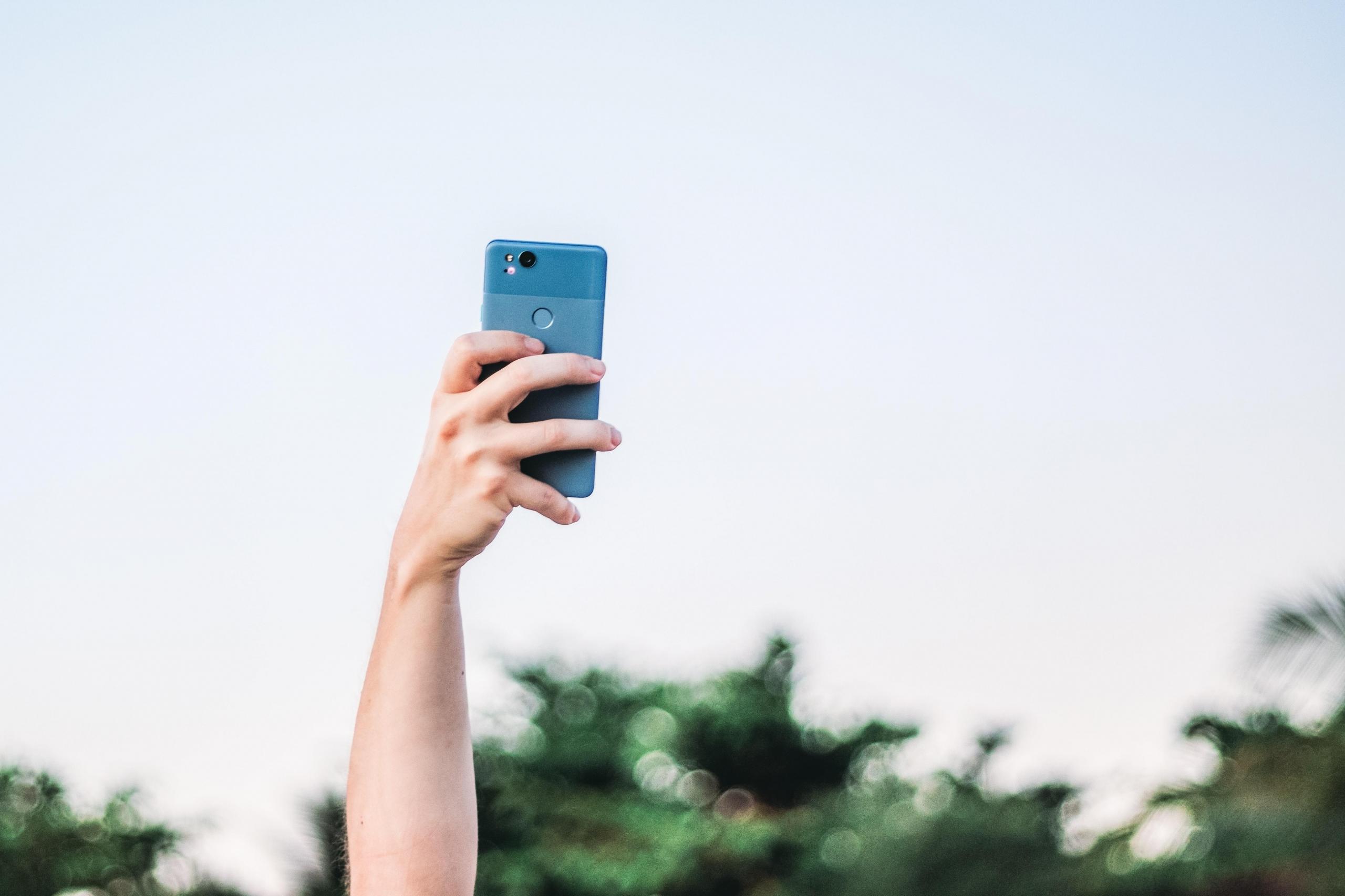 person taking photo with blue cellphone raised above head