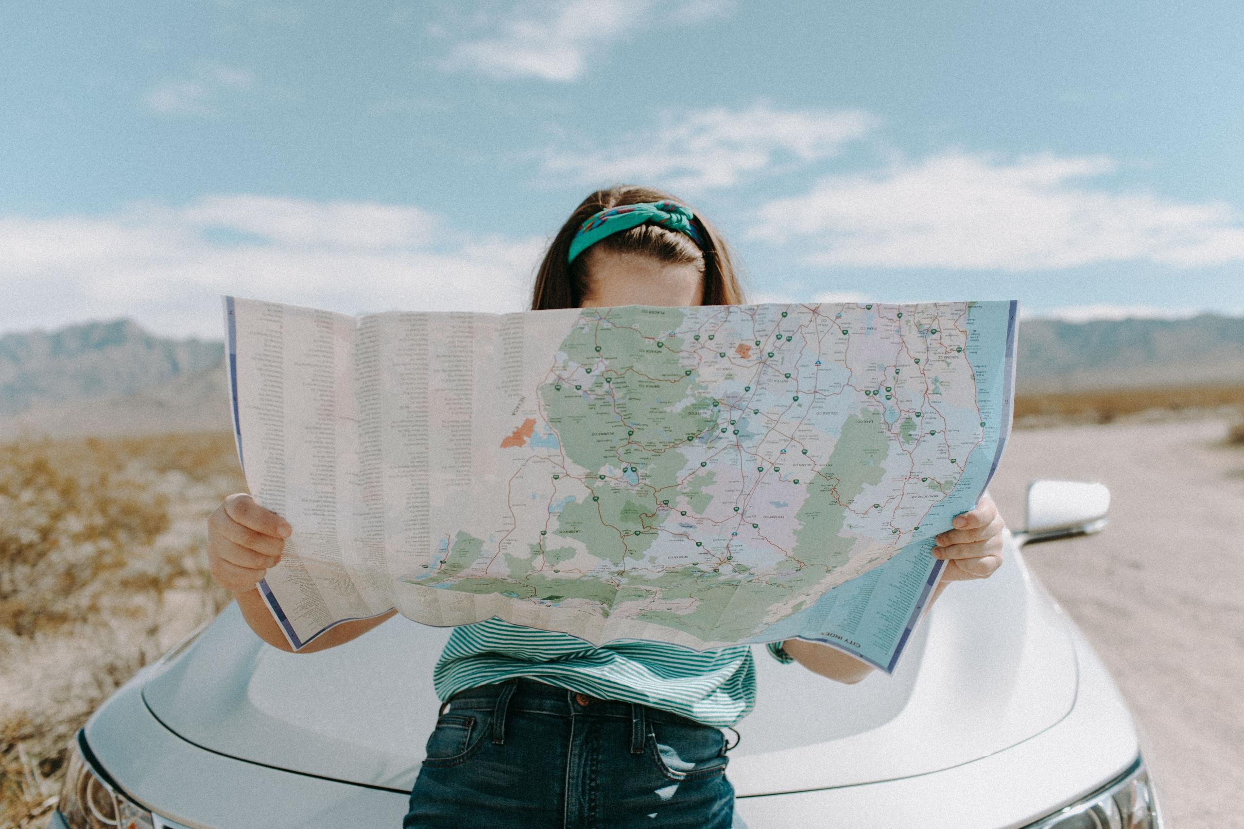 woman sitting on car bonnet consulting a map