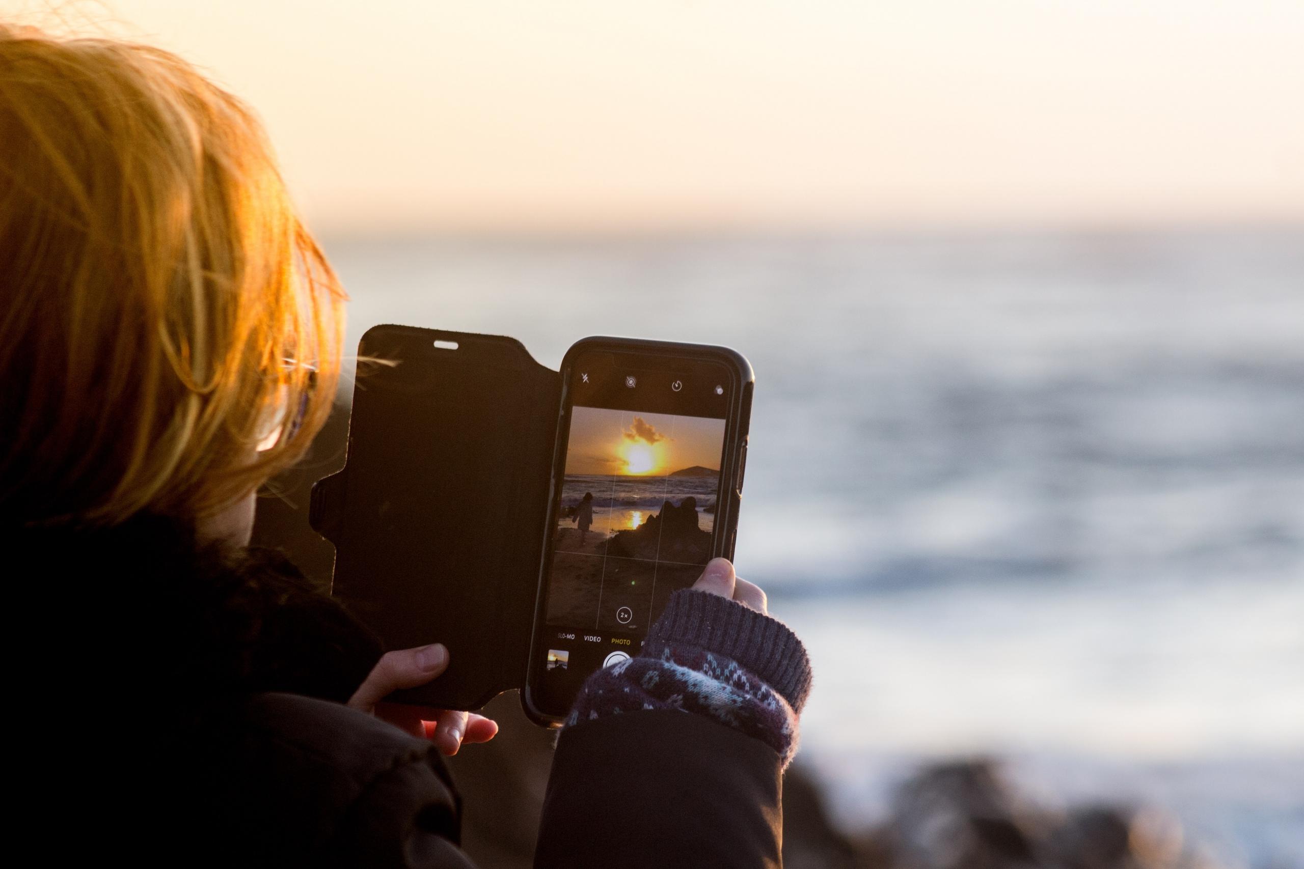 woman photographing sunset over the sea with smartphone camera