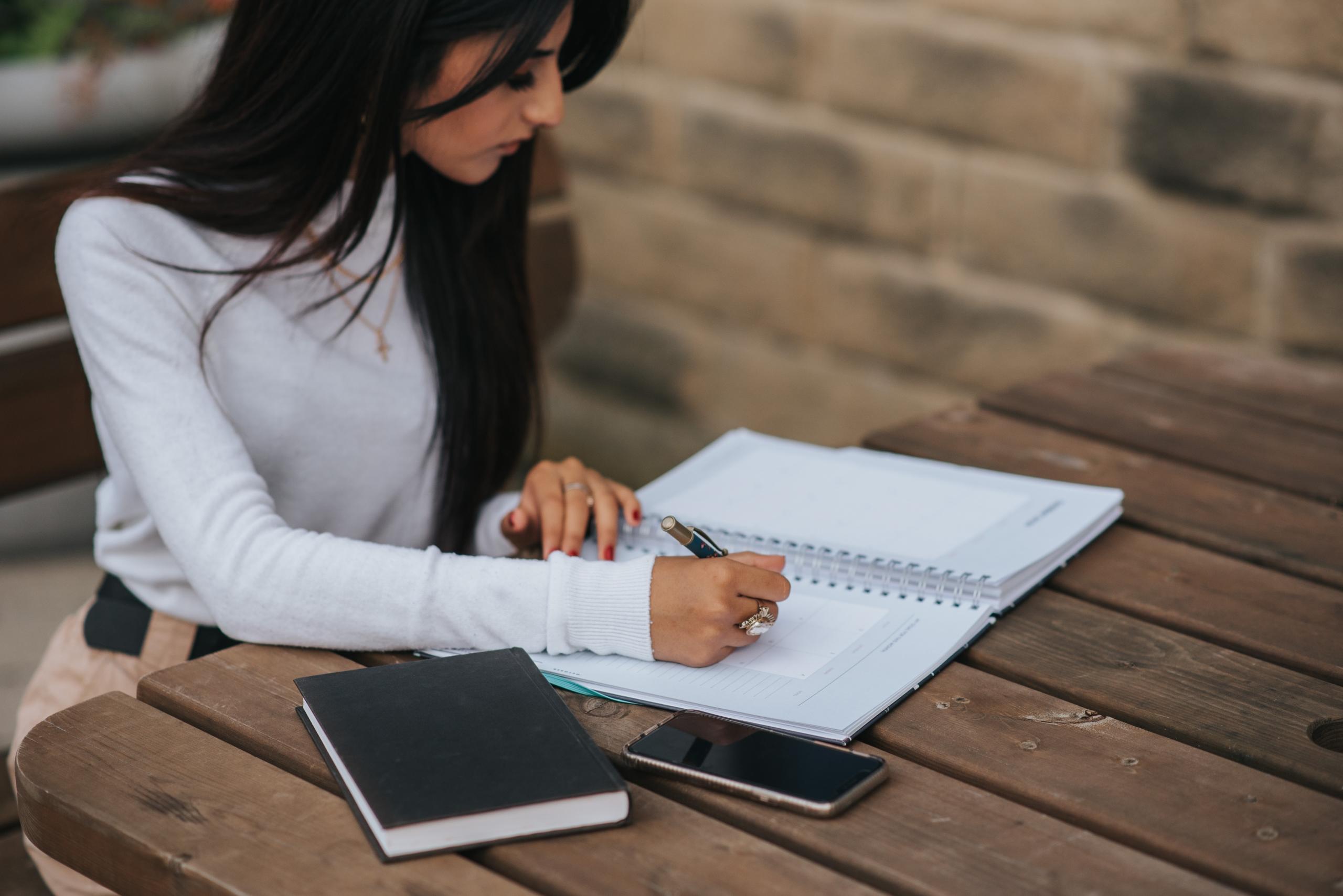 woman seated at desk outdoors writing