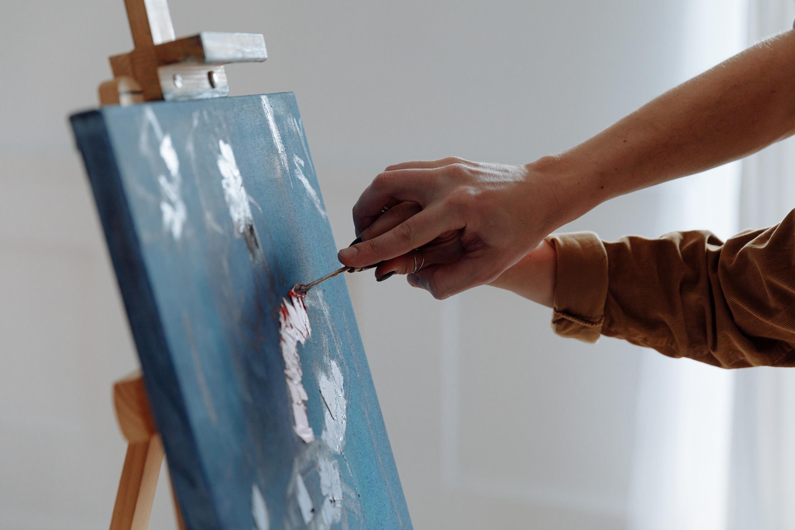 teacher helping art student paint on canvas