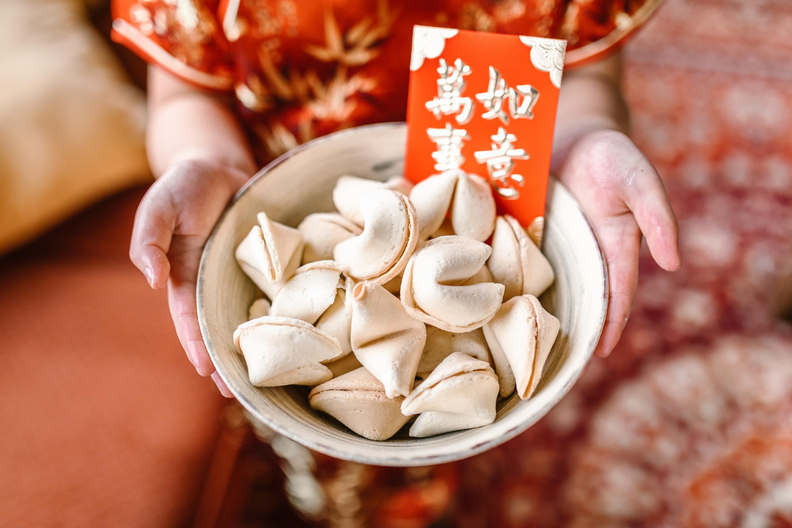 woman holding bowl filled with fortune cookies and red card with Chinese writing