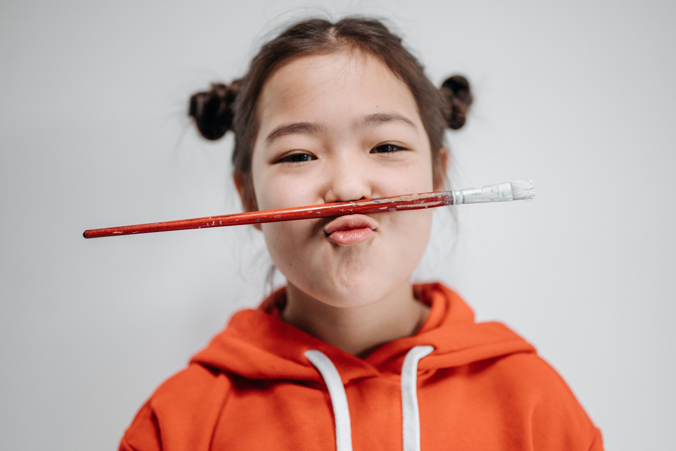 girl balancing red paintbrush between nose and lip