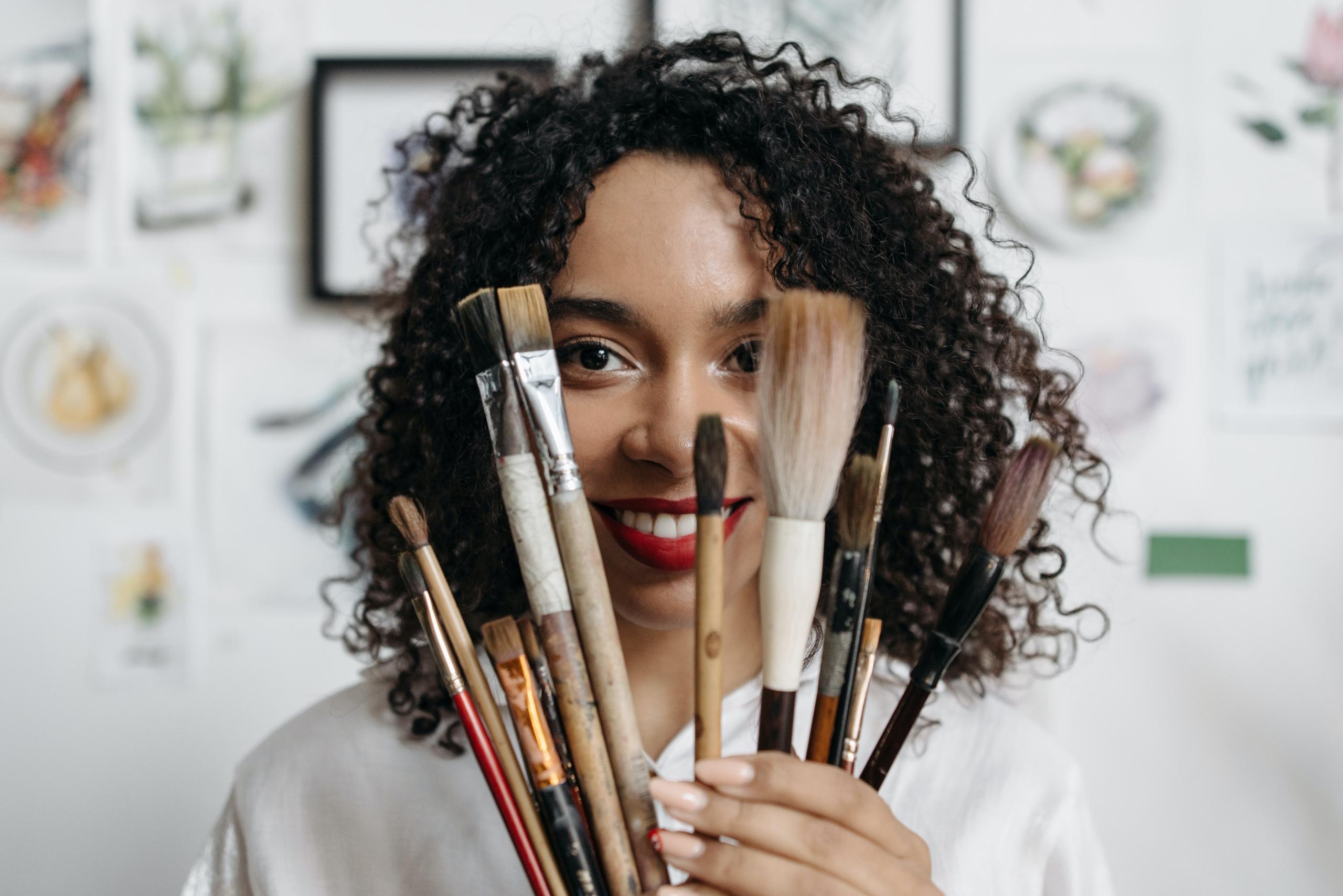 woman with paintbrushes fanned out in front of face