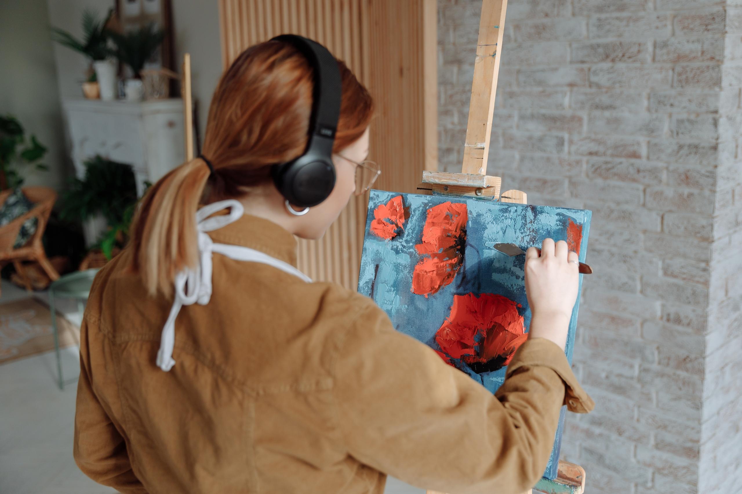 woman creating art on canvas while wearing headphones