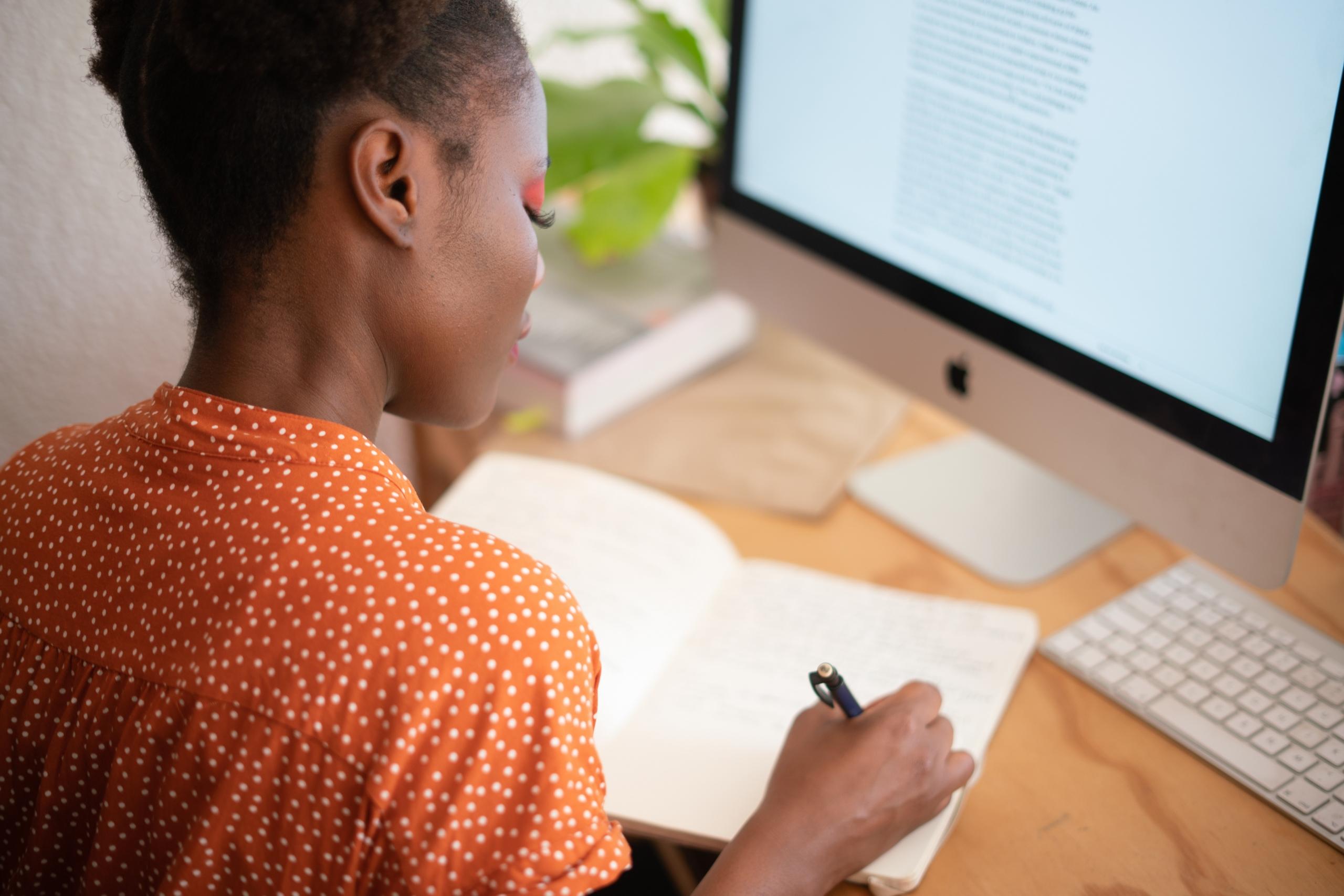 woman writing in notebook and using desktop computer