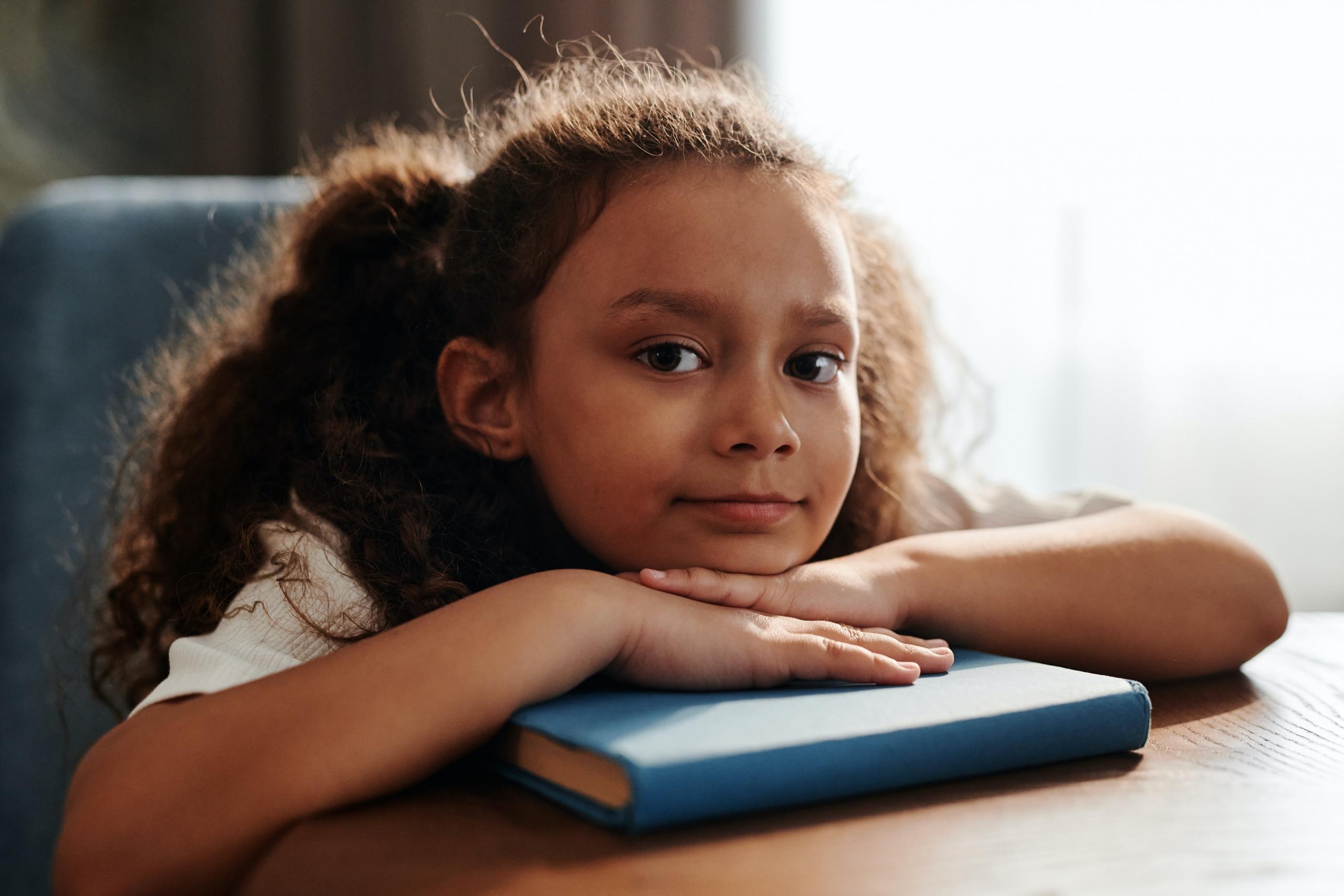 little girl with book placed on table in front of her