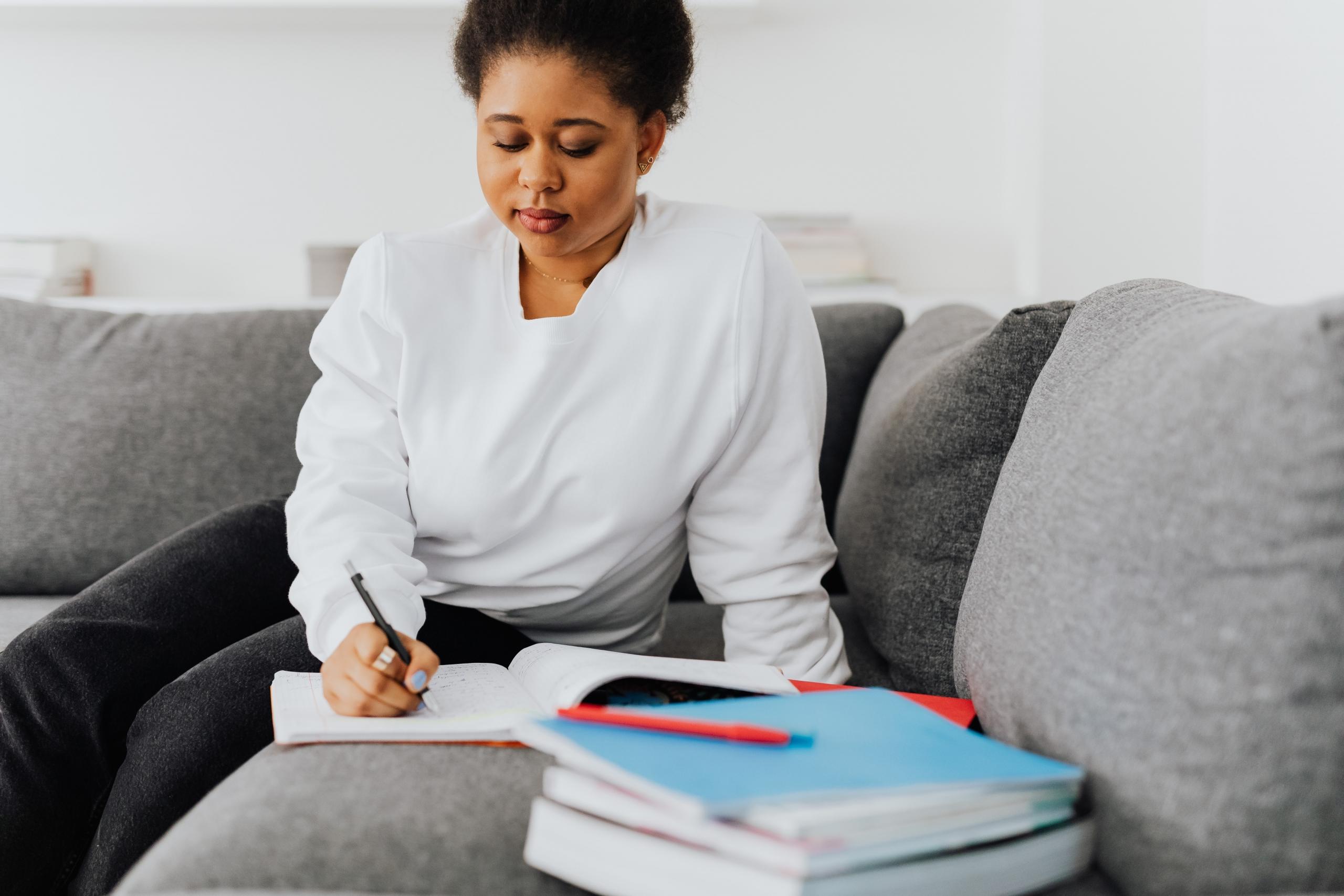 person writing in notebook behind a pile of textbooks