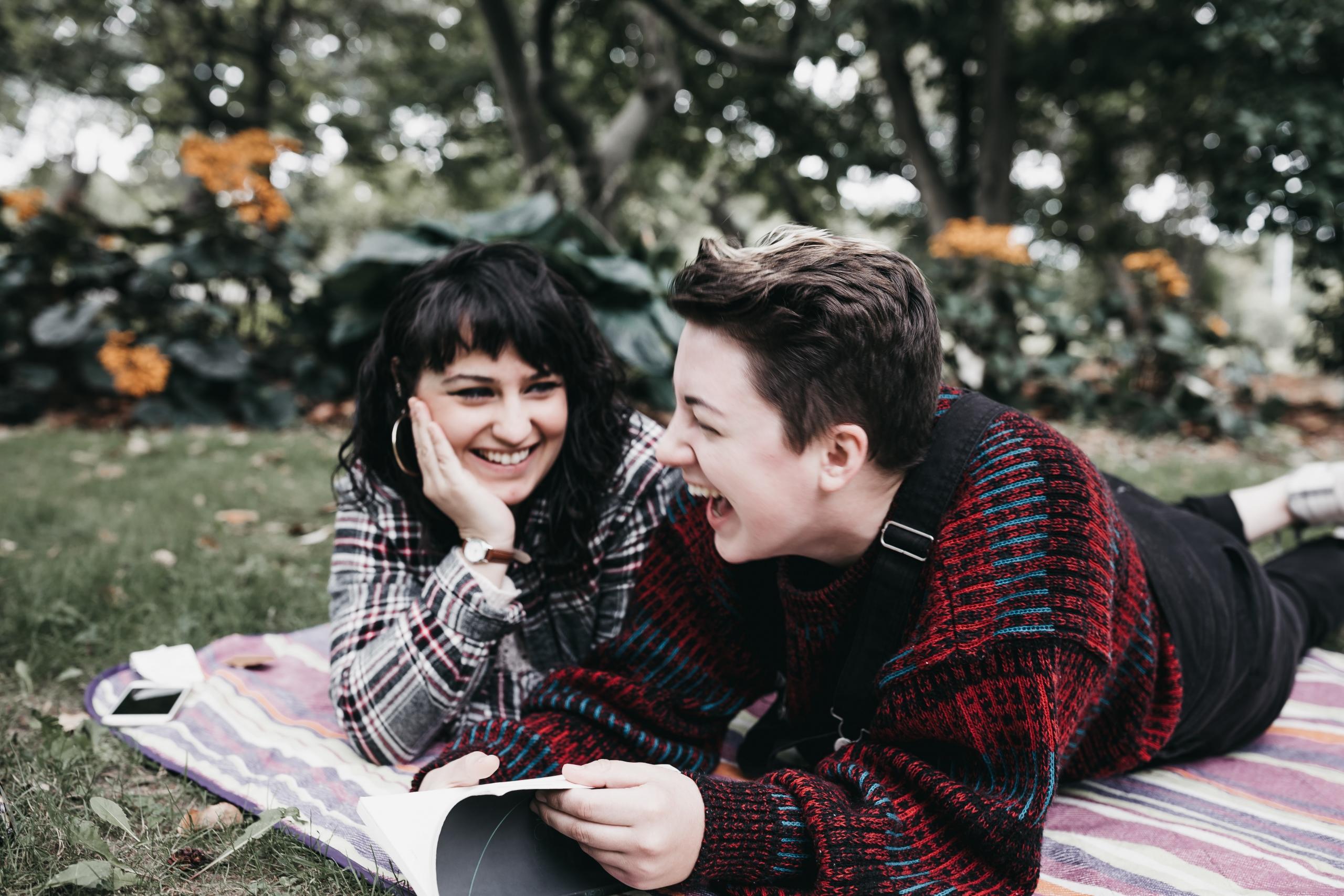 couple reading a book and laughing on picnic blanket