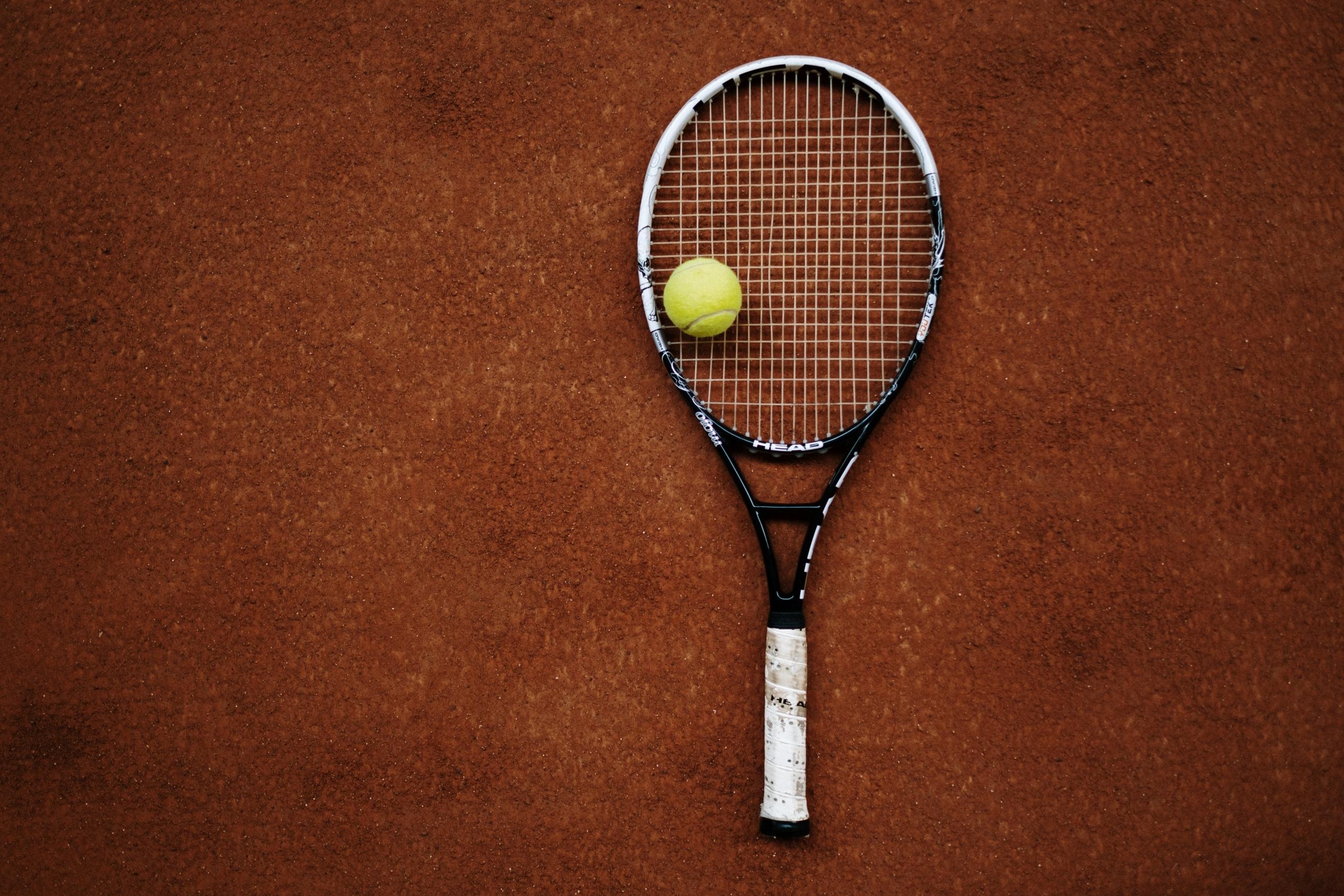 tennis ball placed on racket on clay court
