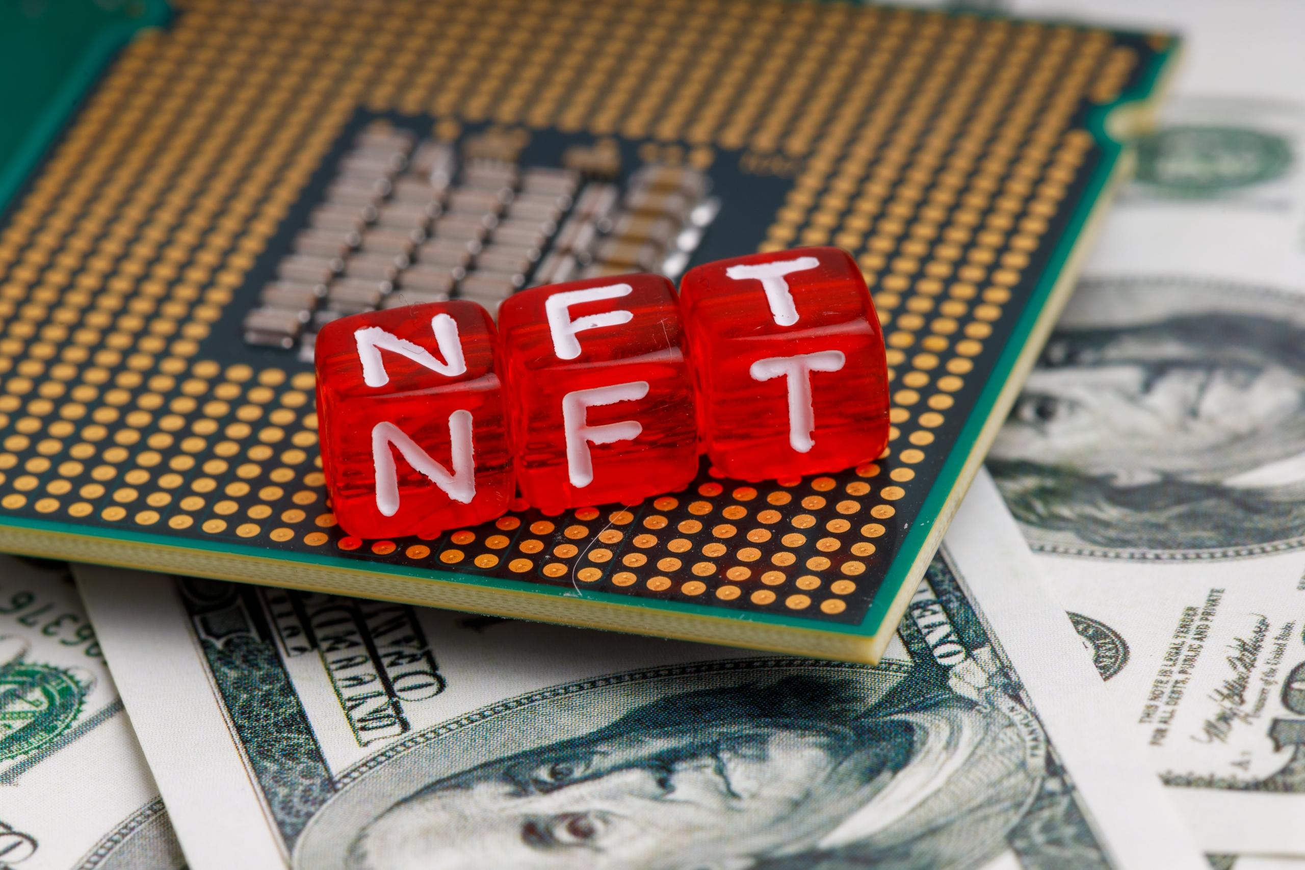 letter blocks spelling out nft atop pile of money