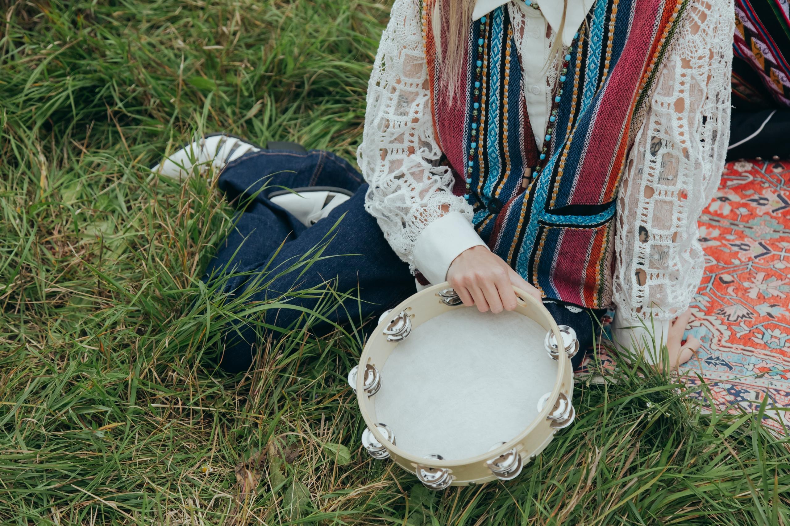 person sitting on grass playing tambourine instrument