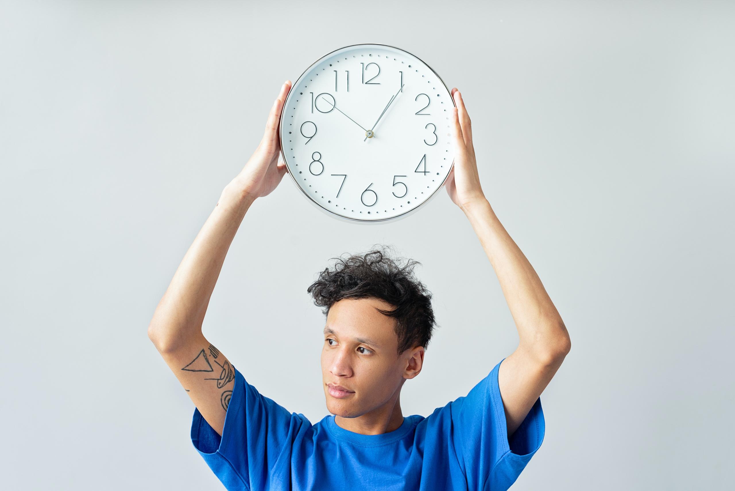 person in blue t-shirt with clock held in raised hands