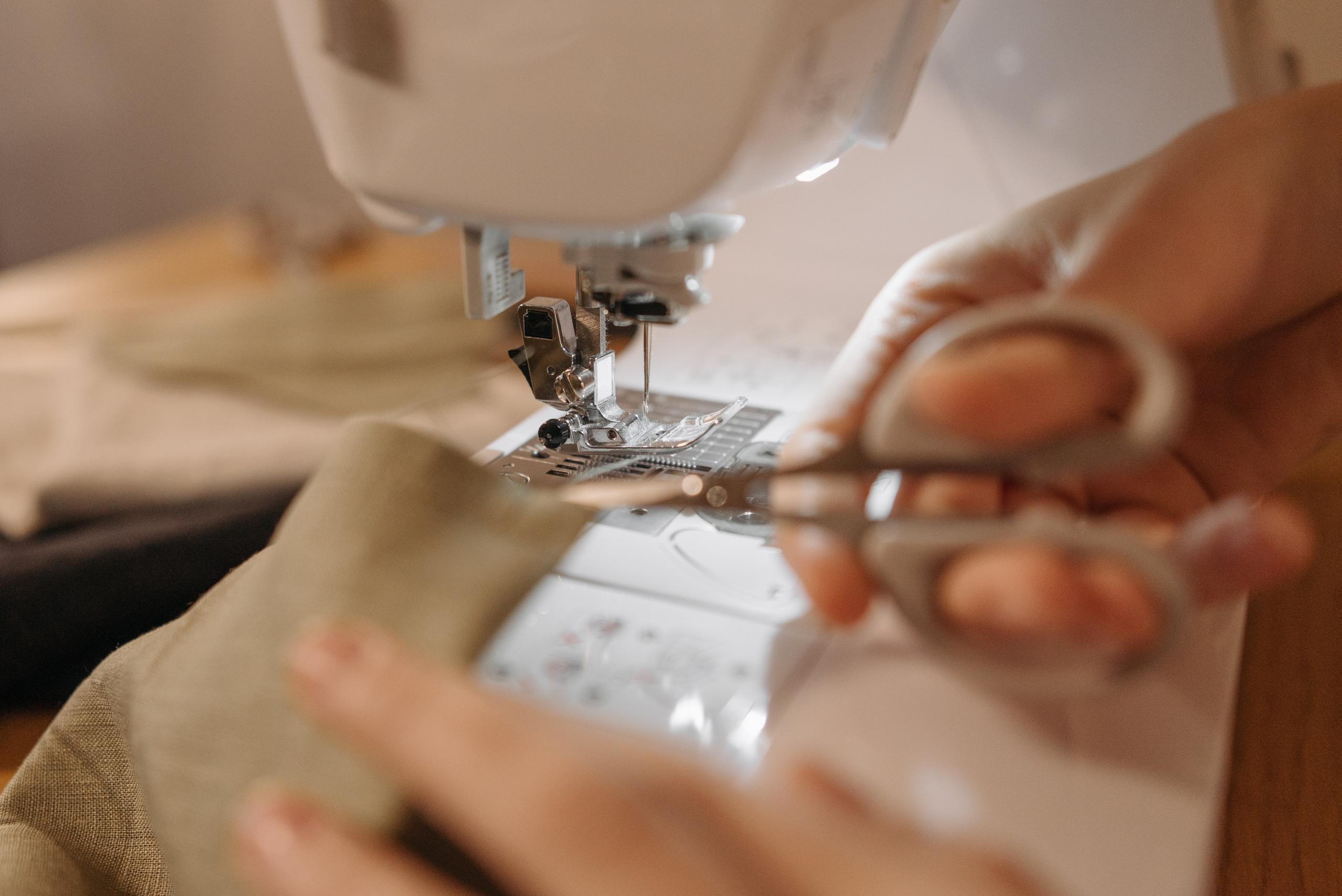 woman using sewing machine and trimming fabric with dressmaker's scissors