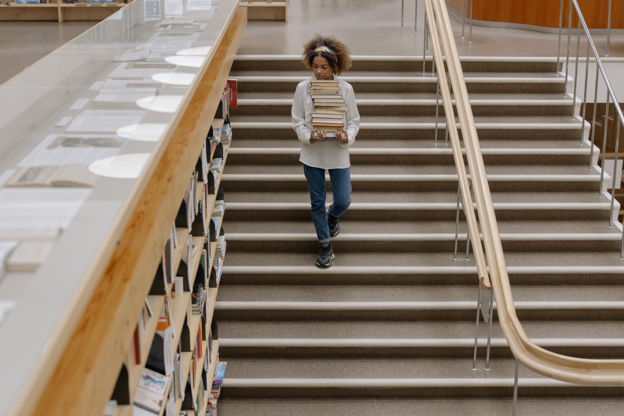woman carrying pile of books in a library
