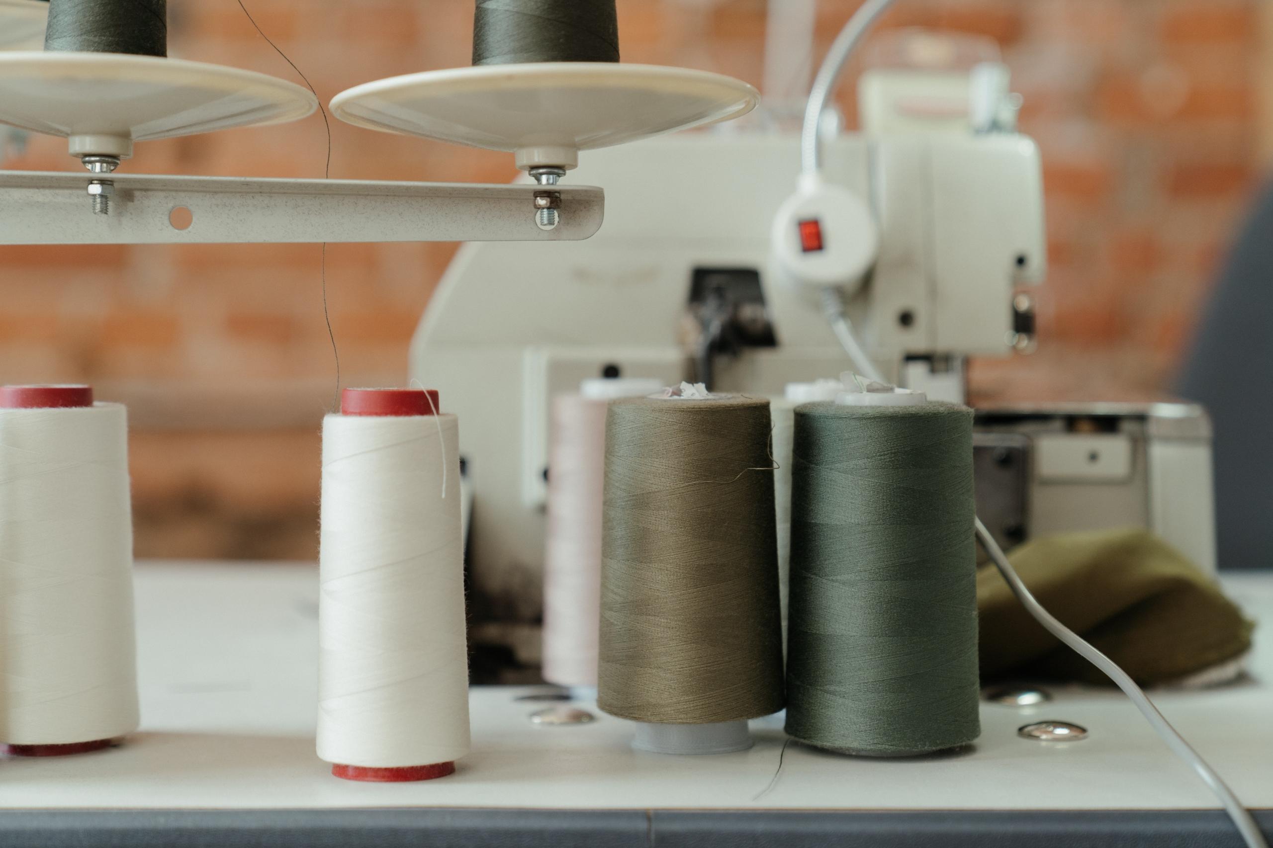 bobbins of different coloured cotton thread next to sewing machine