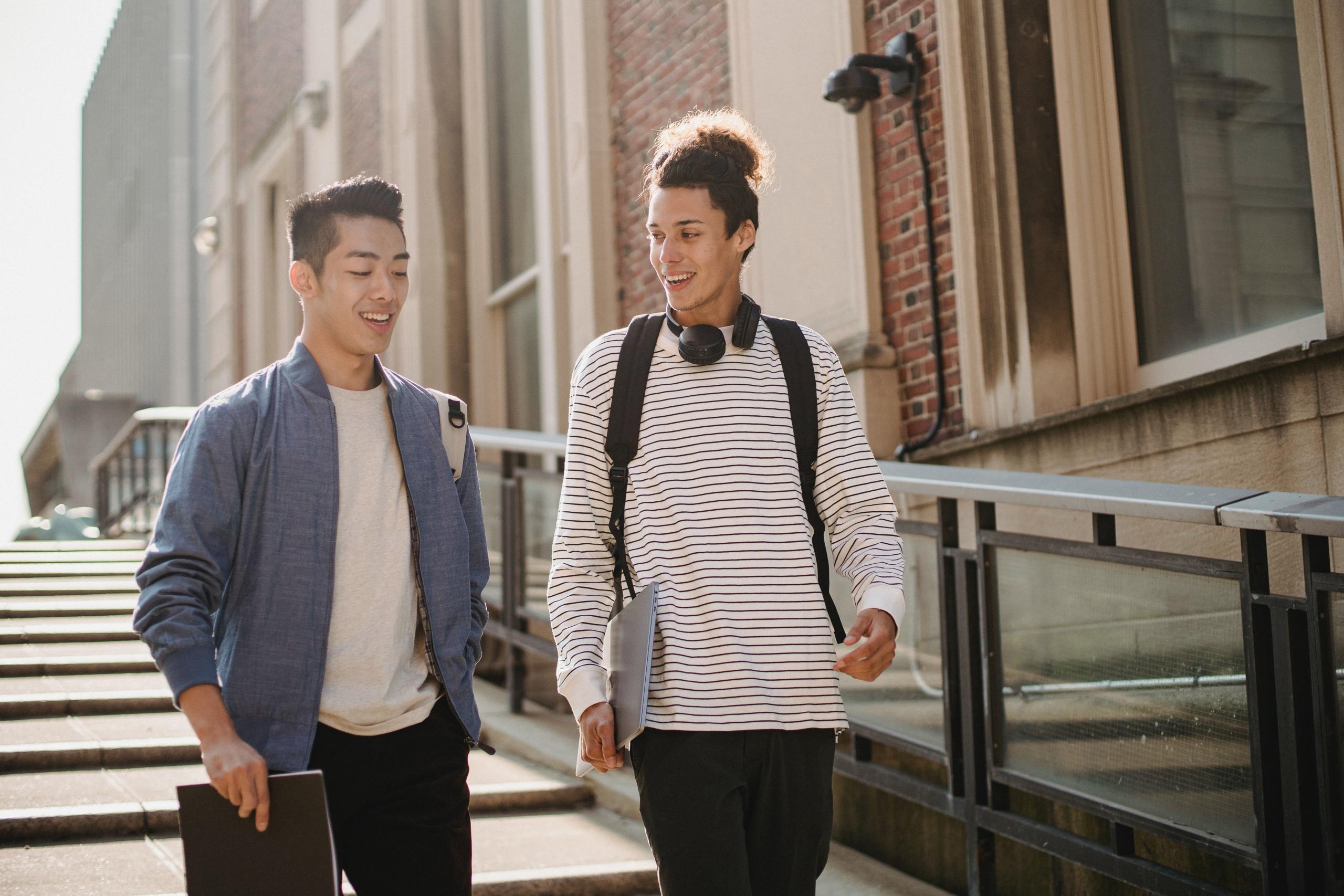 two students carrying a notebook and laptop