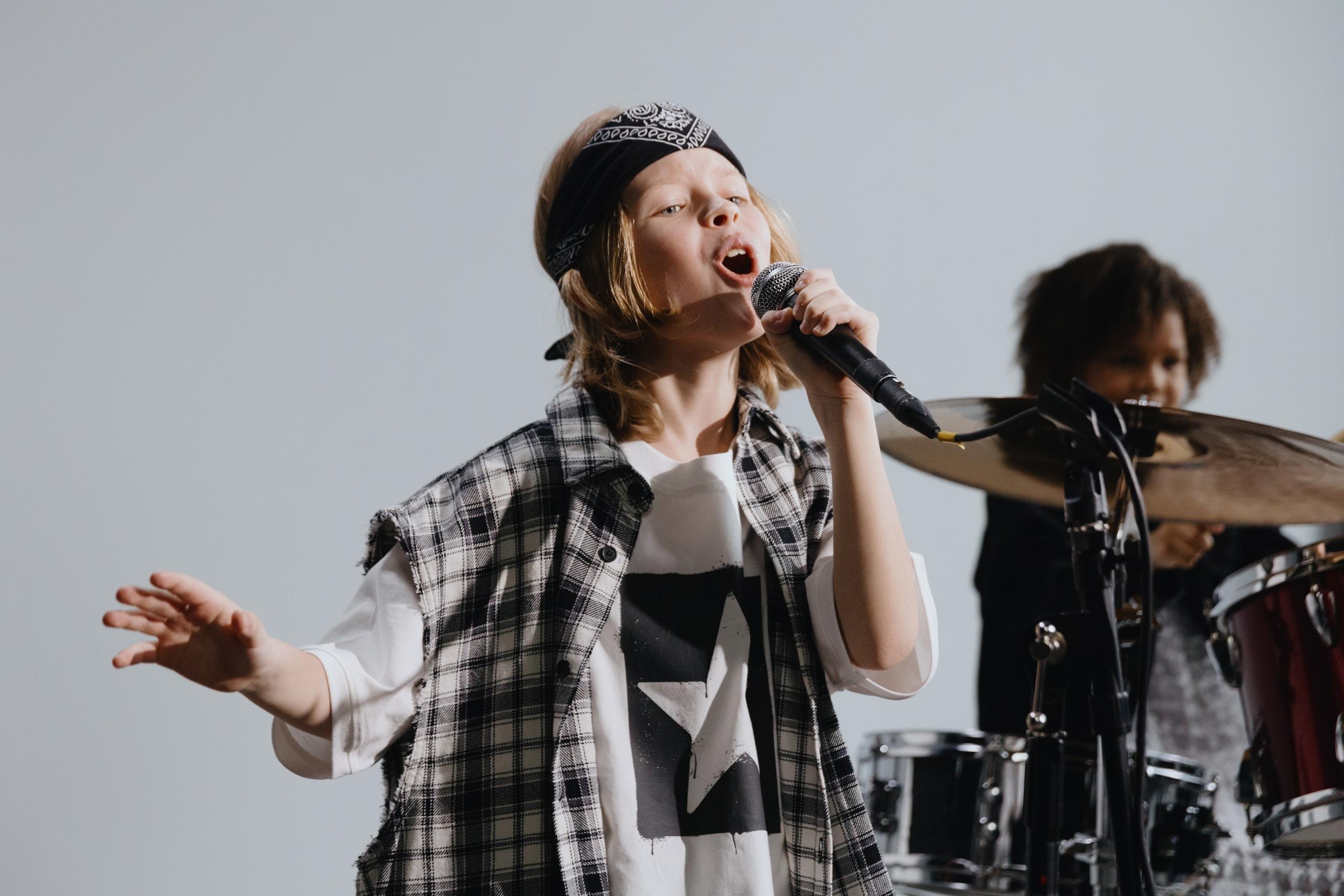 boy singing into mic while another plays the drums