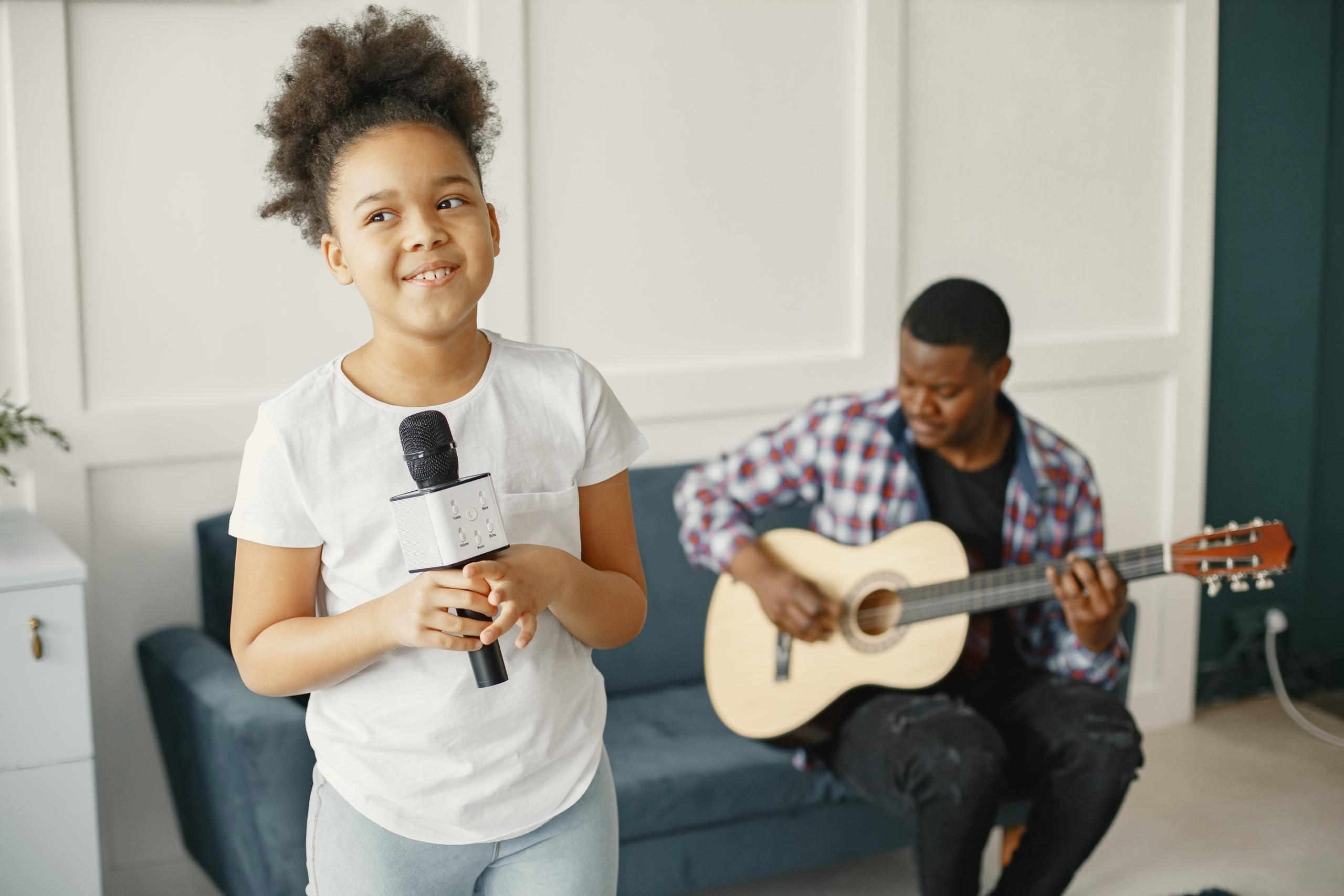 young singing student holding microphone whilst teacher plays guitar