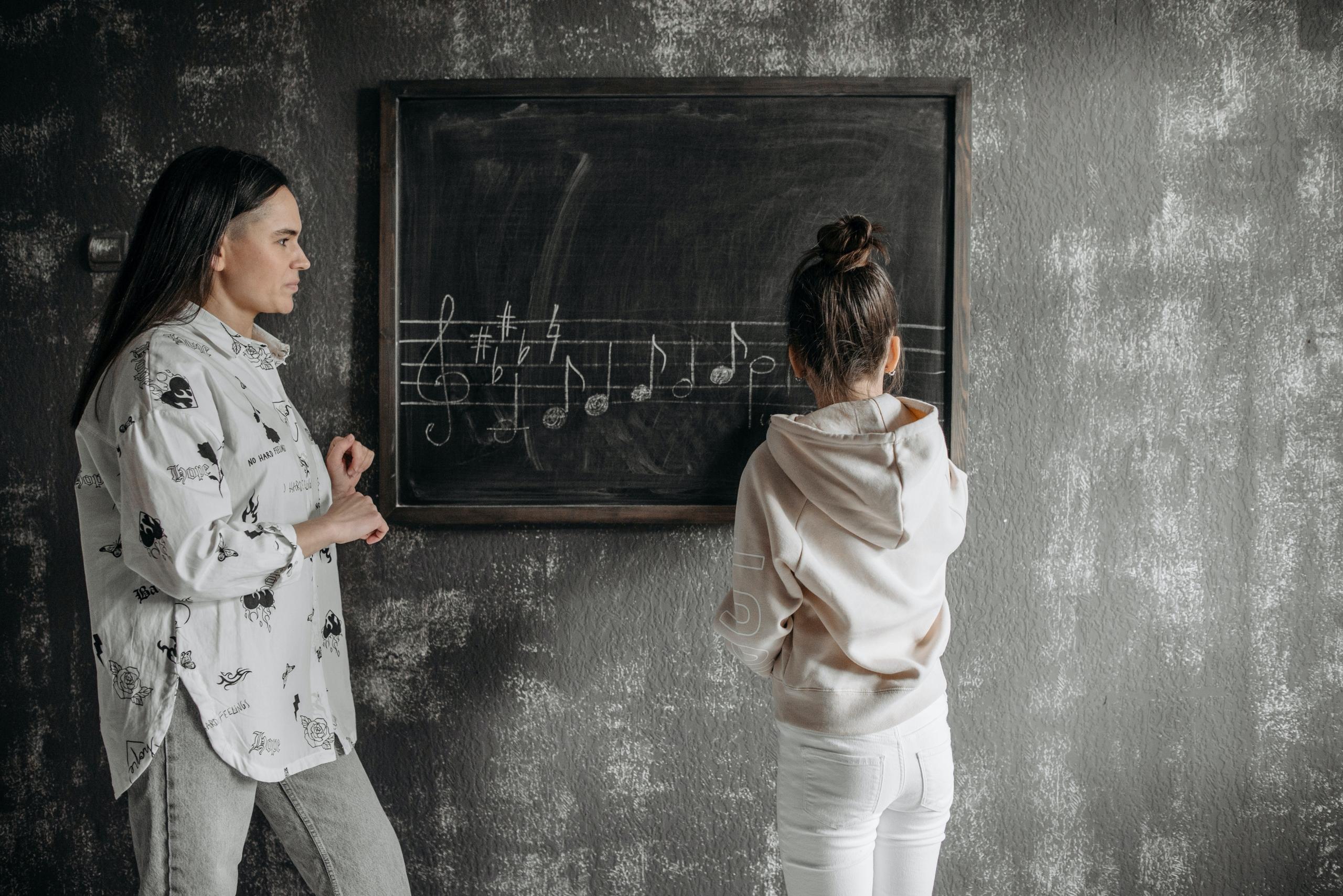 music teacher teaching child to write musical notes on a blackboard