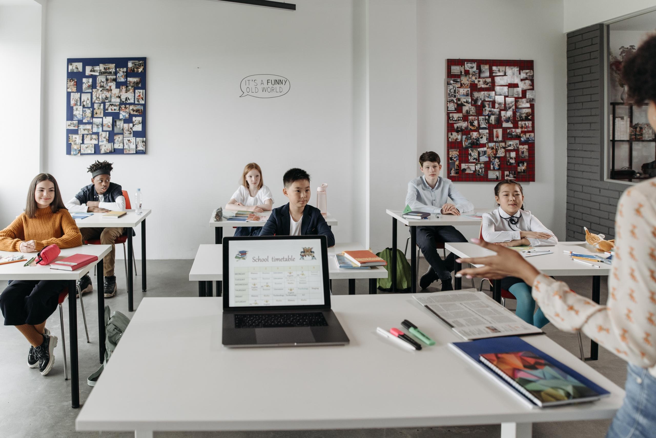 school children seated at desks listening to teacher talk