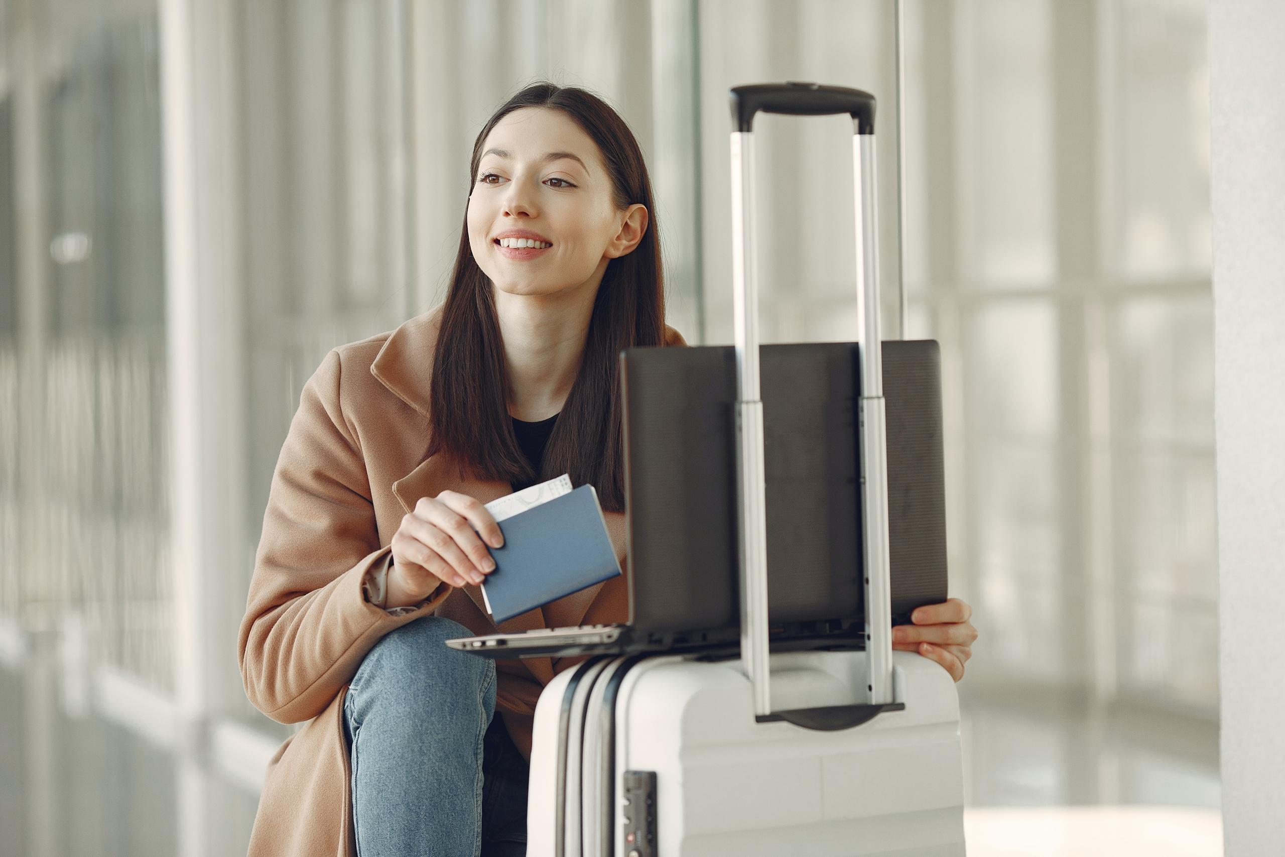 woman with carry on luggage, laptop and passport in airport corridor