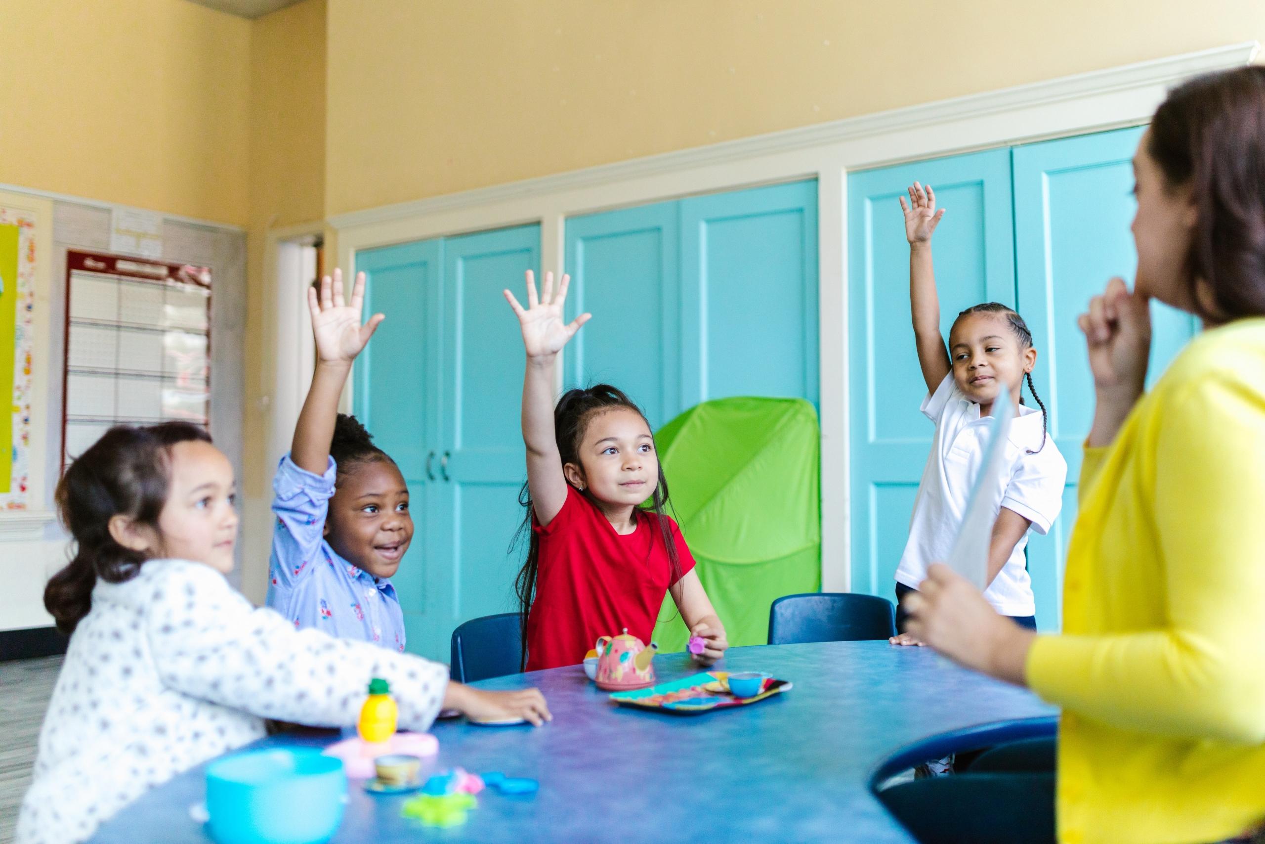 pre-school kids raising hands as teacher asks question