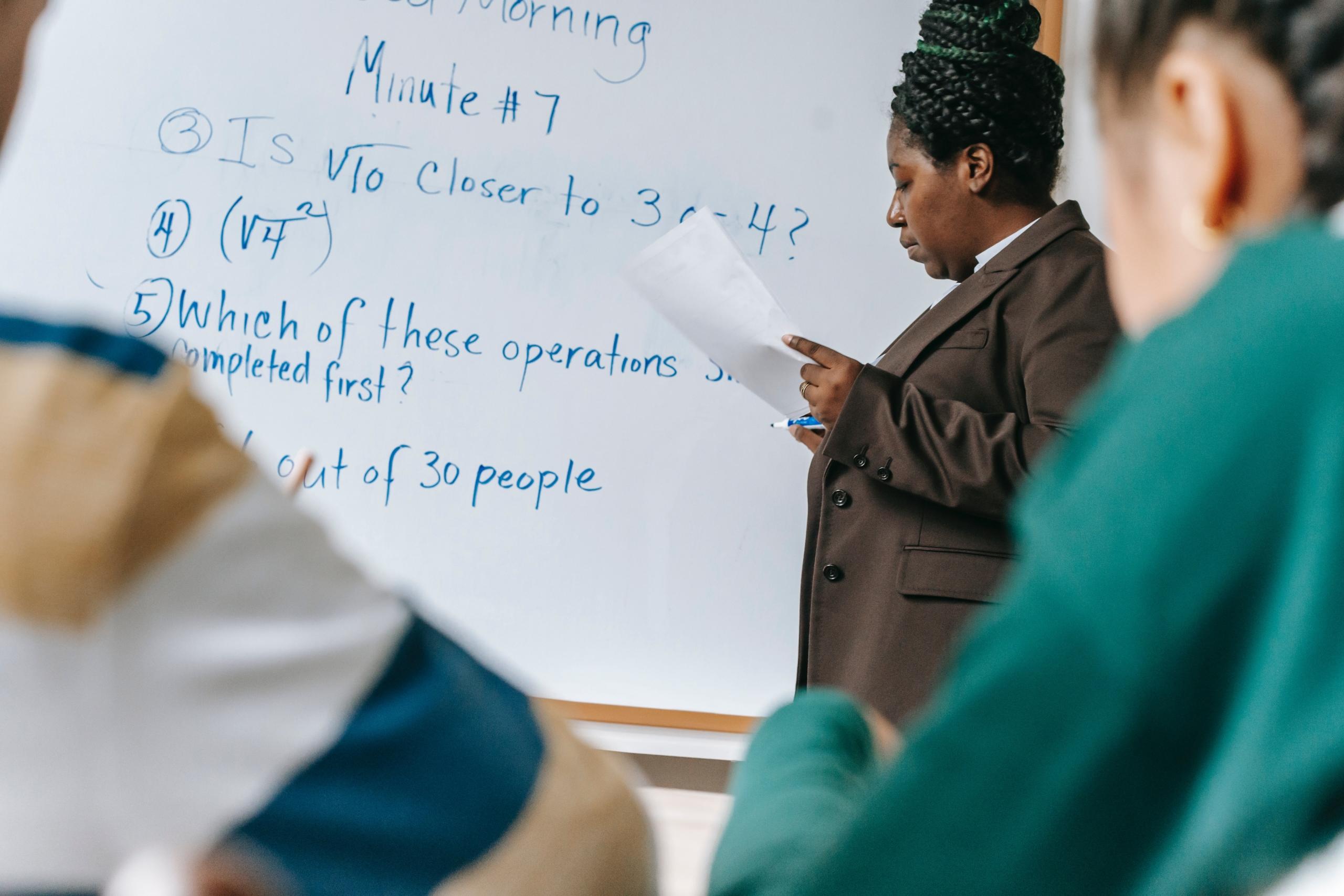 teacher writing maths equations on whiteboard