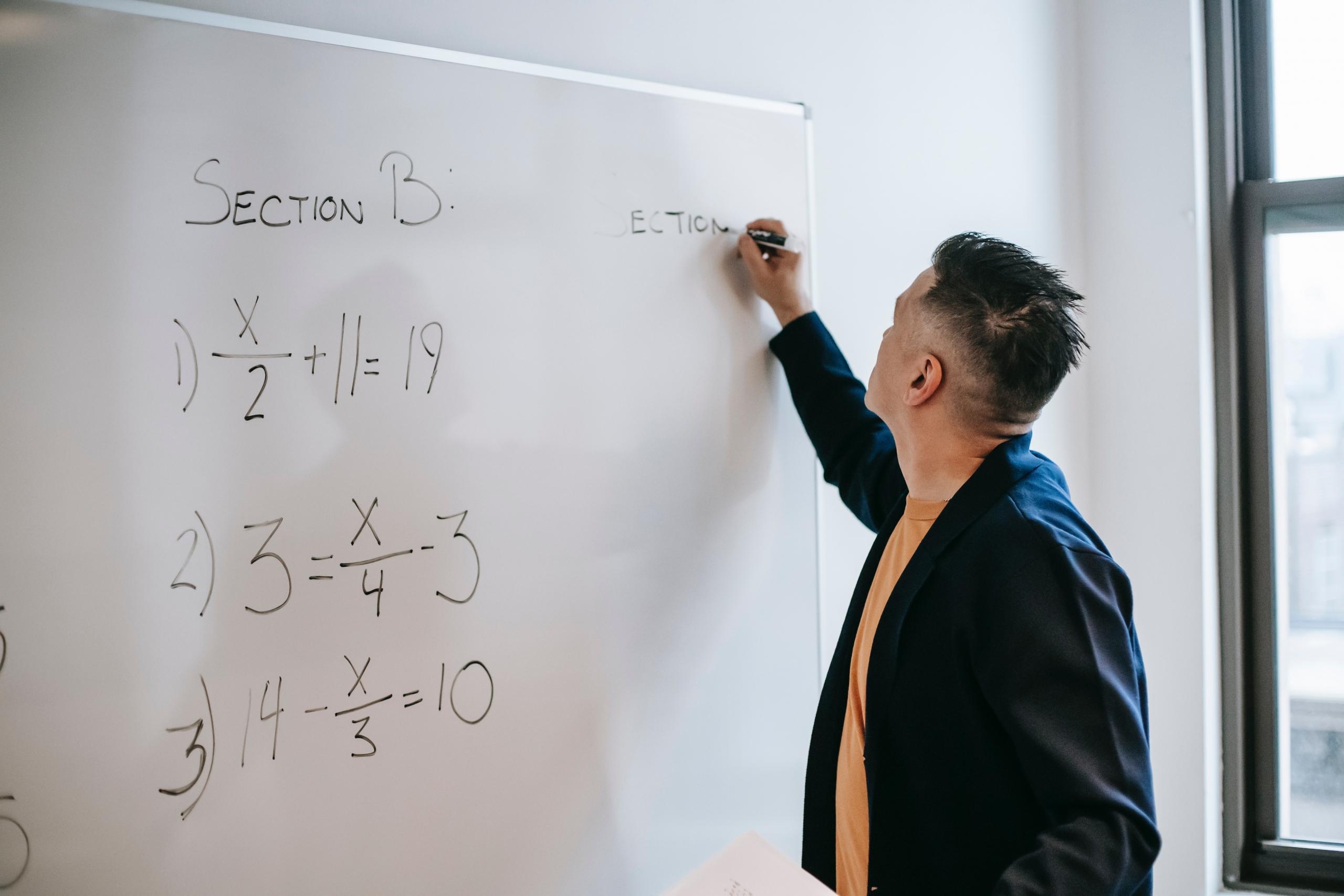 teacher writing maths problems on a board